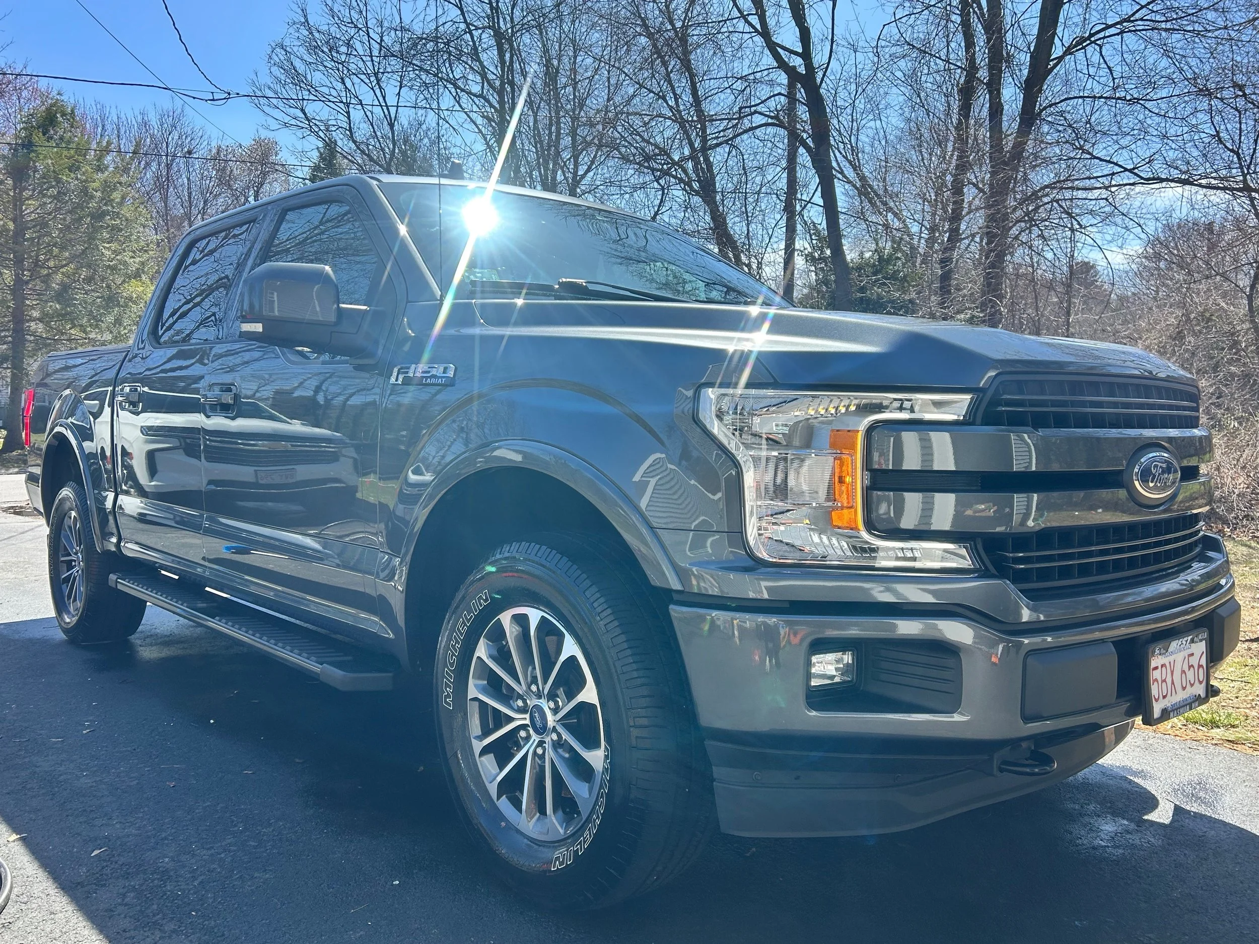 Black Ford F-150 pickup truck parked outdoors on a sunny day, with trees and a clear blue sky in the background.