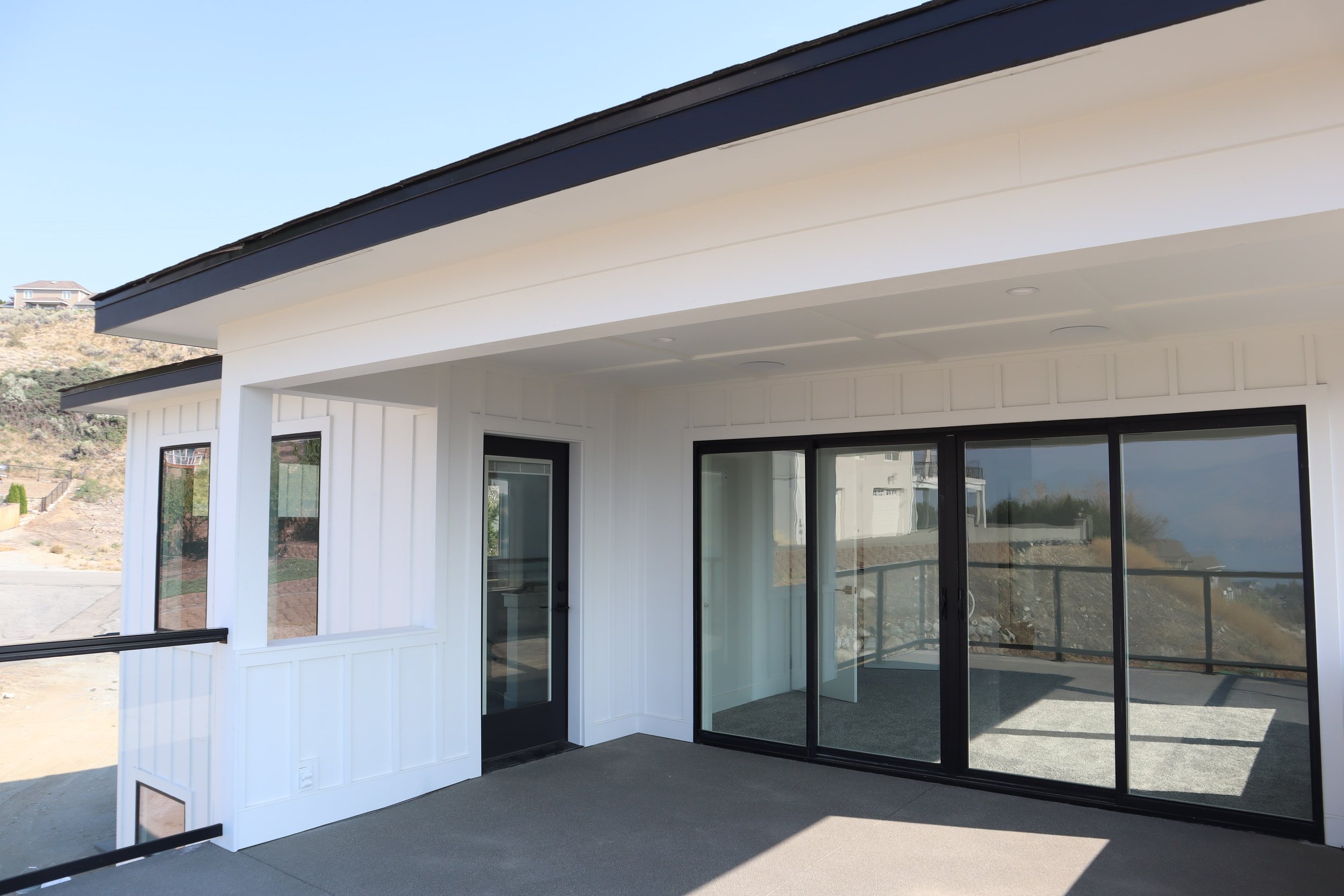 Modern house exterior with white board-and-batten siding, large glass sliding doors, and covered porch.