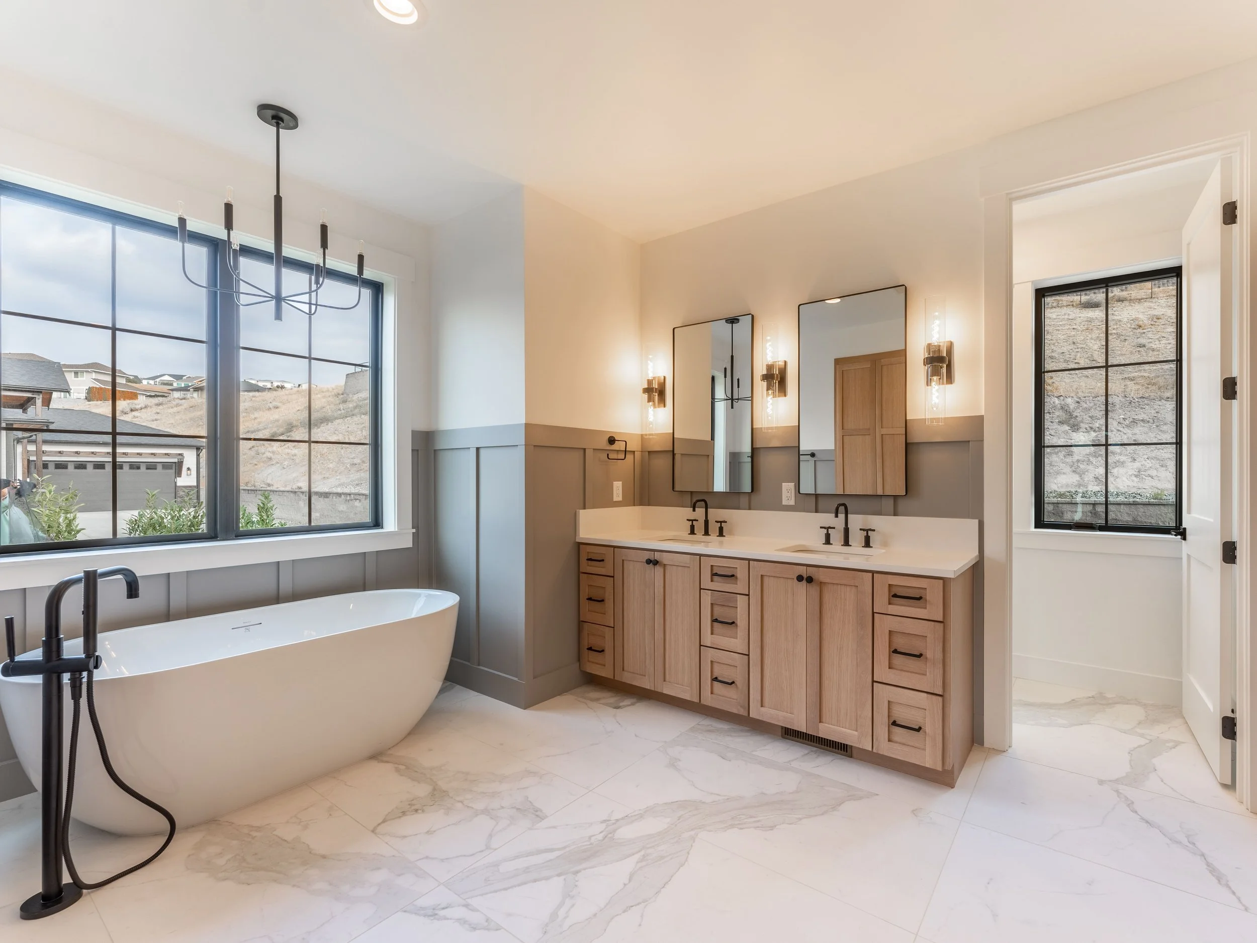 Modern bathroom with freestanding bathtub, double vanity with mirrors, and elegant lighting.