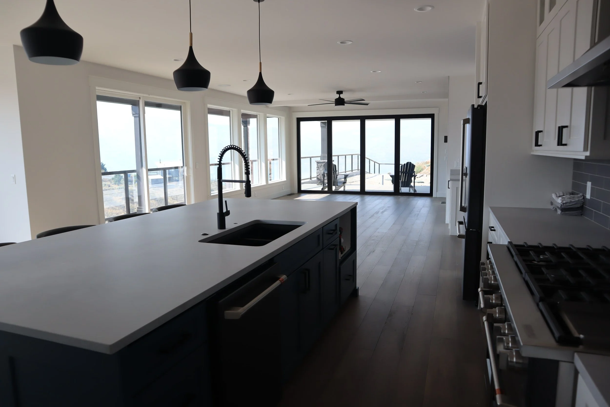 Modern kitchen with large island, black fixtures, pendant lights, and glass doors leading to a patio with outdoor seating.