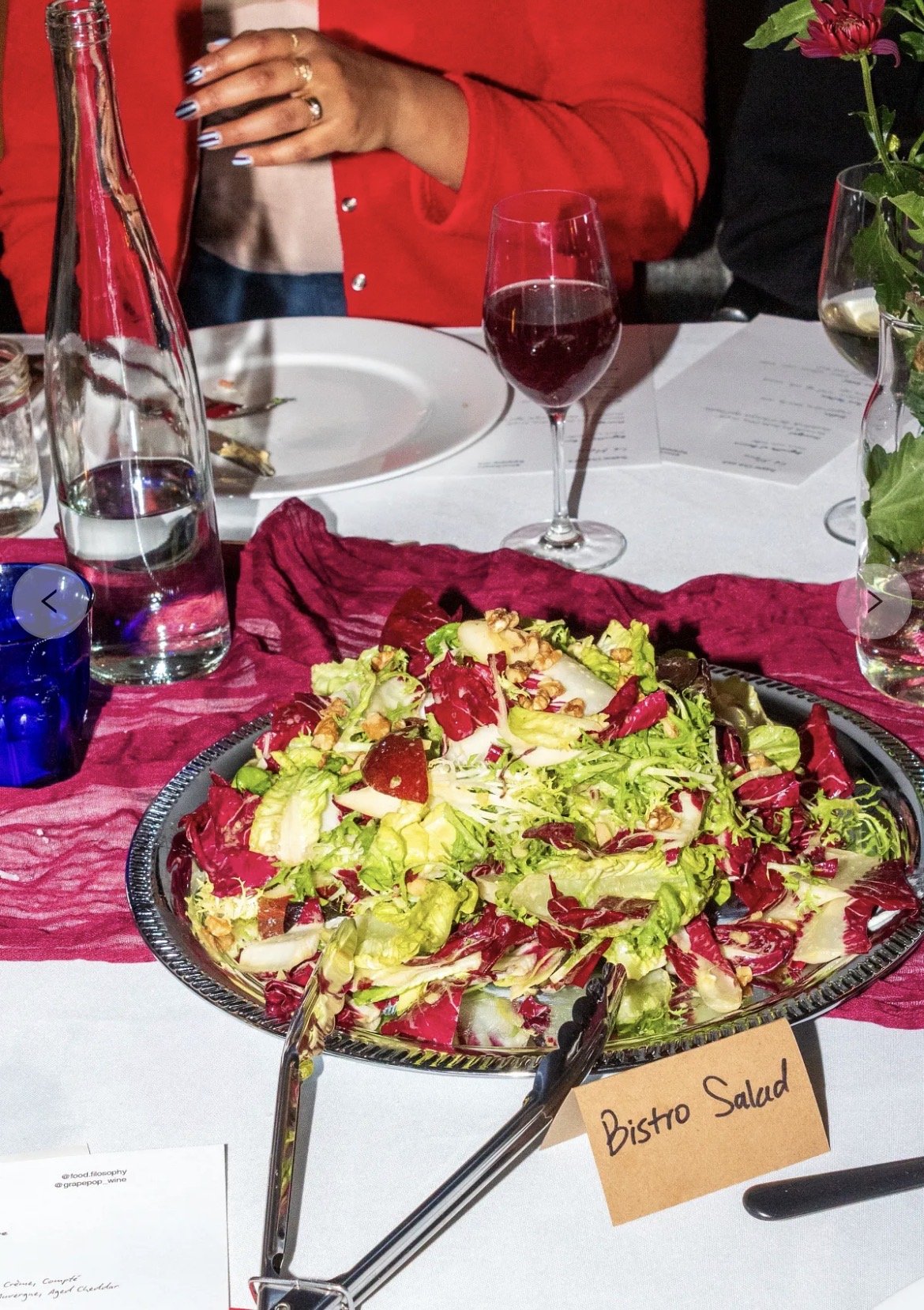 A salad tray with mixed greens labeled 'Bistro Salad' on a dining table at a restaurant or event.