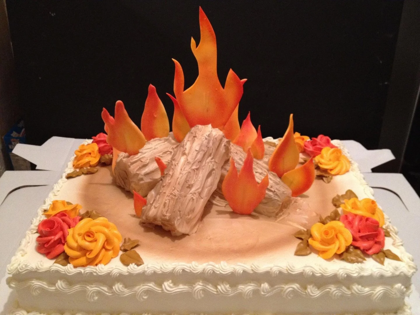 Cake decorated with edible flames, faux logs, and floral piping, resembling a campfire.