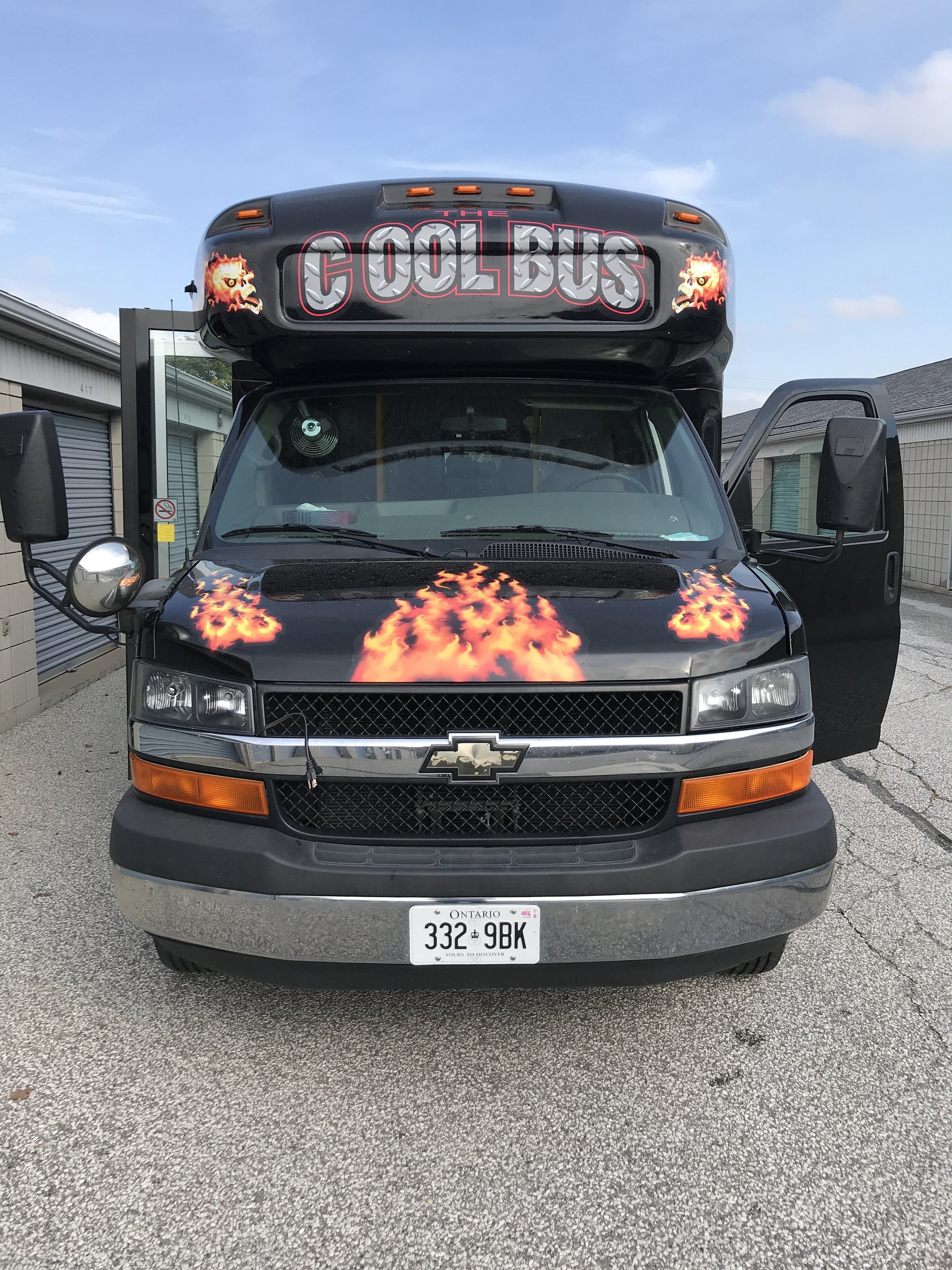 Black bus with "COOL BUS" sign and flame decals, parked outdoors.