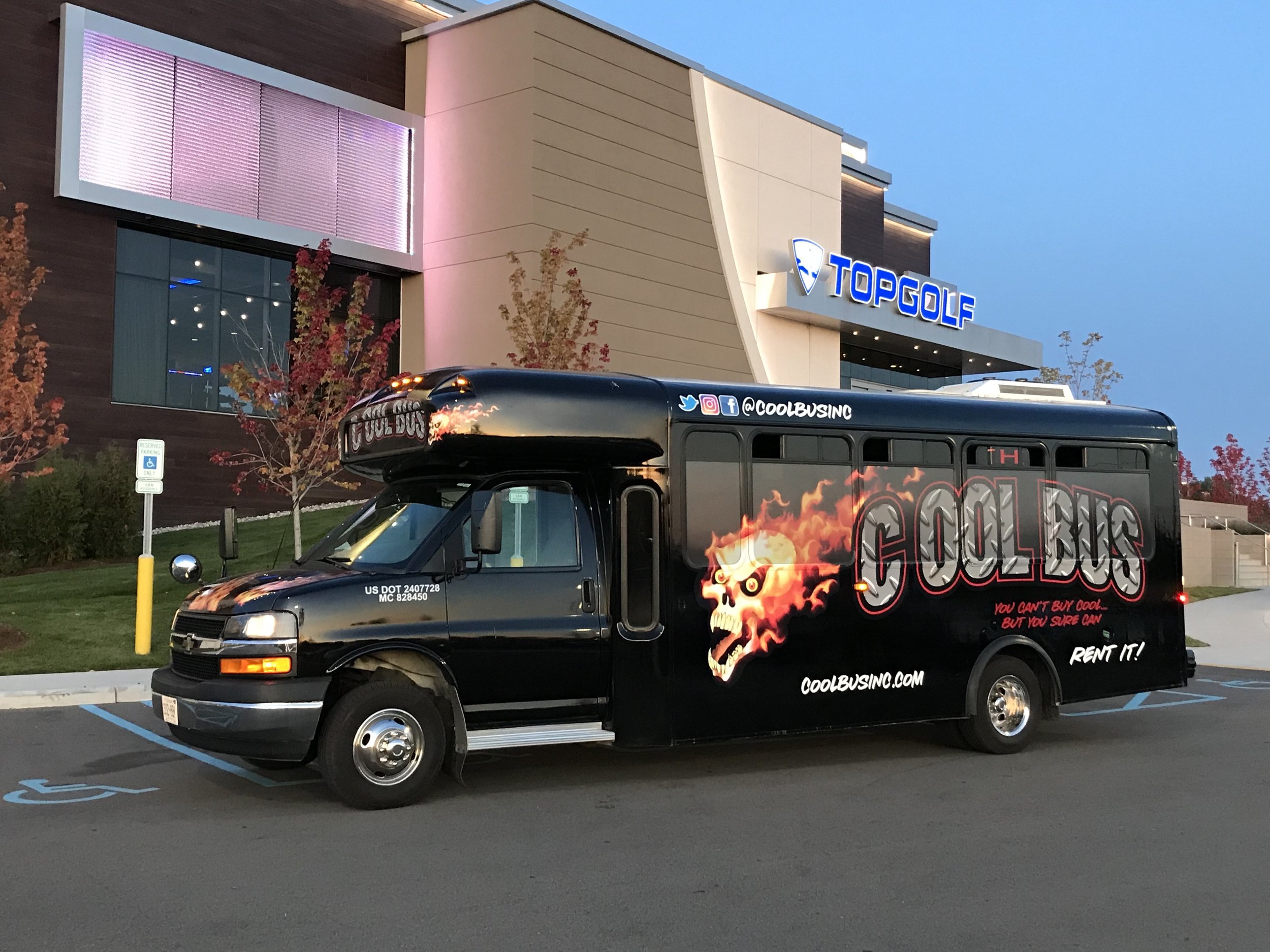 Black bus with 'Cool Bus' graphics and flames parked outside Topgolf building.