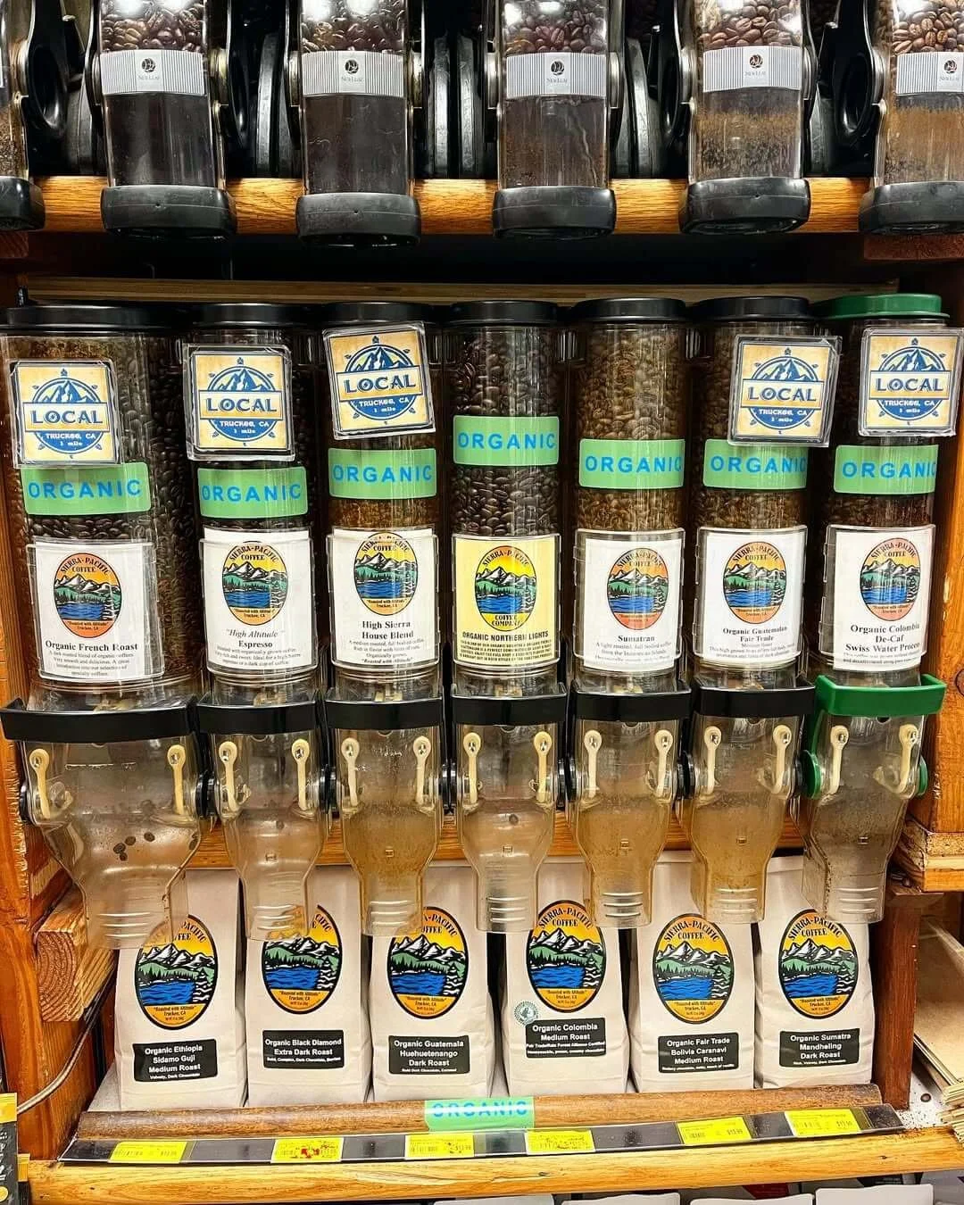 Bulk coffee beans in dispensers and bags in a grocery store, with labels indicating organic and various regions of origin.