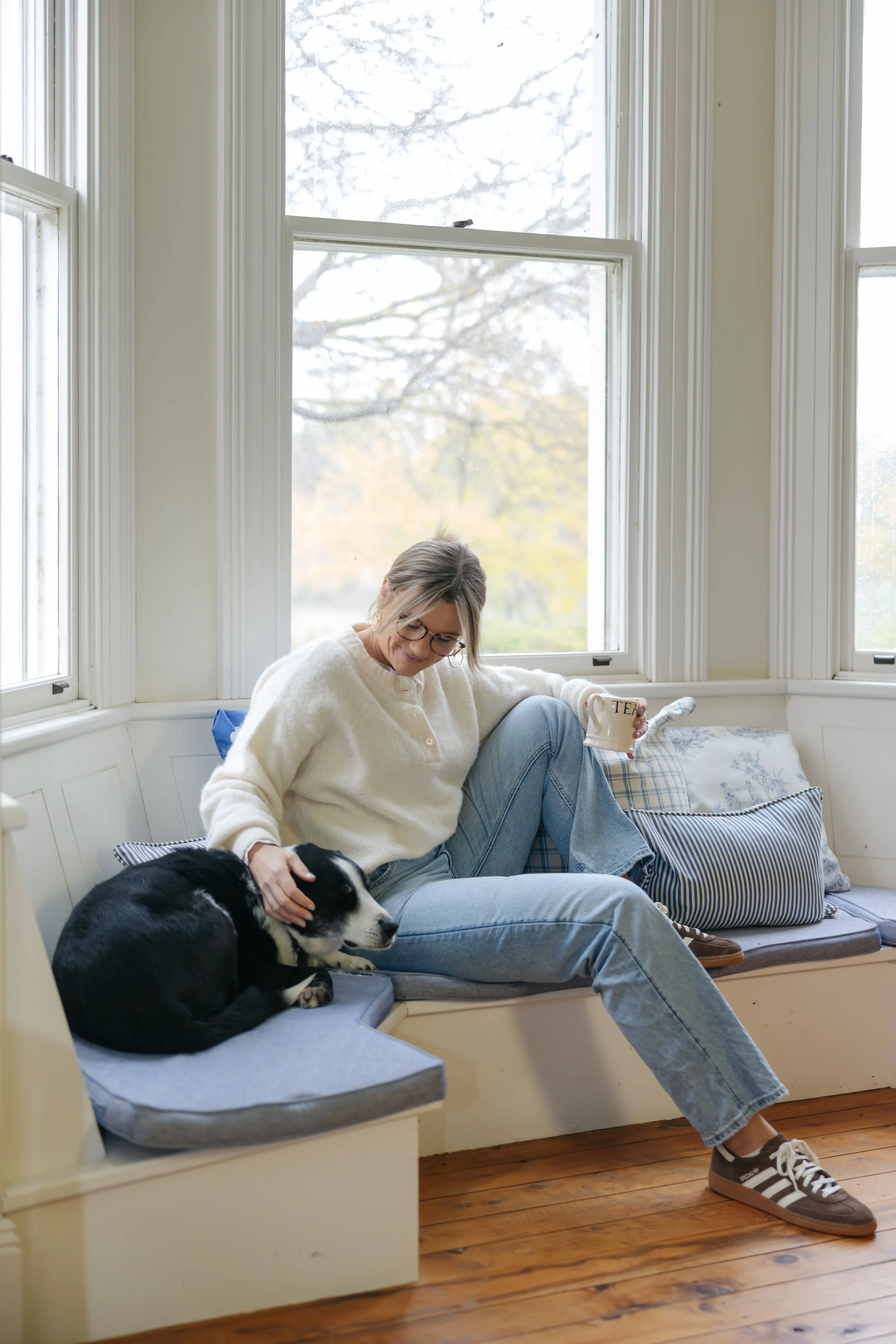 Millie Hardie sitting in a sunlit window nook with Bear her therapy dog, reflecting the safe and welcoming space offered by Millie Hardie Psychology for people of all ages
