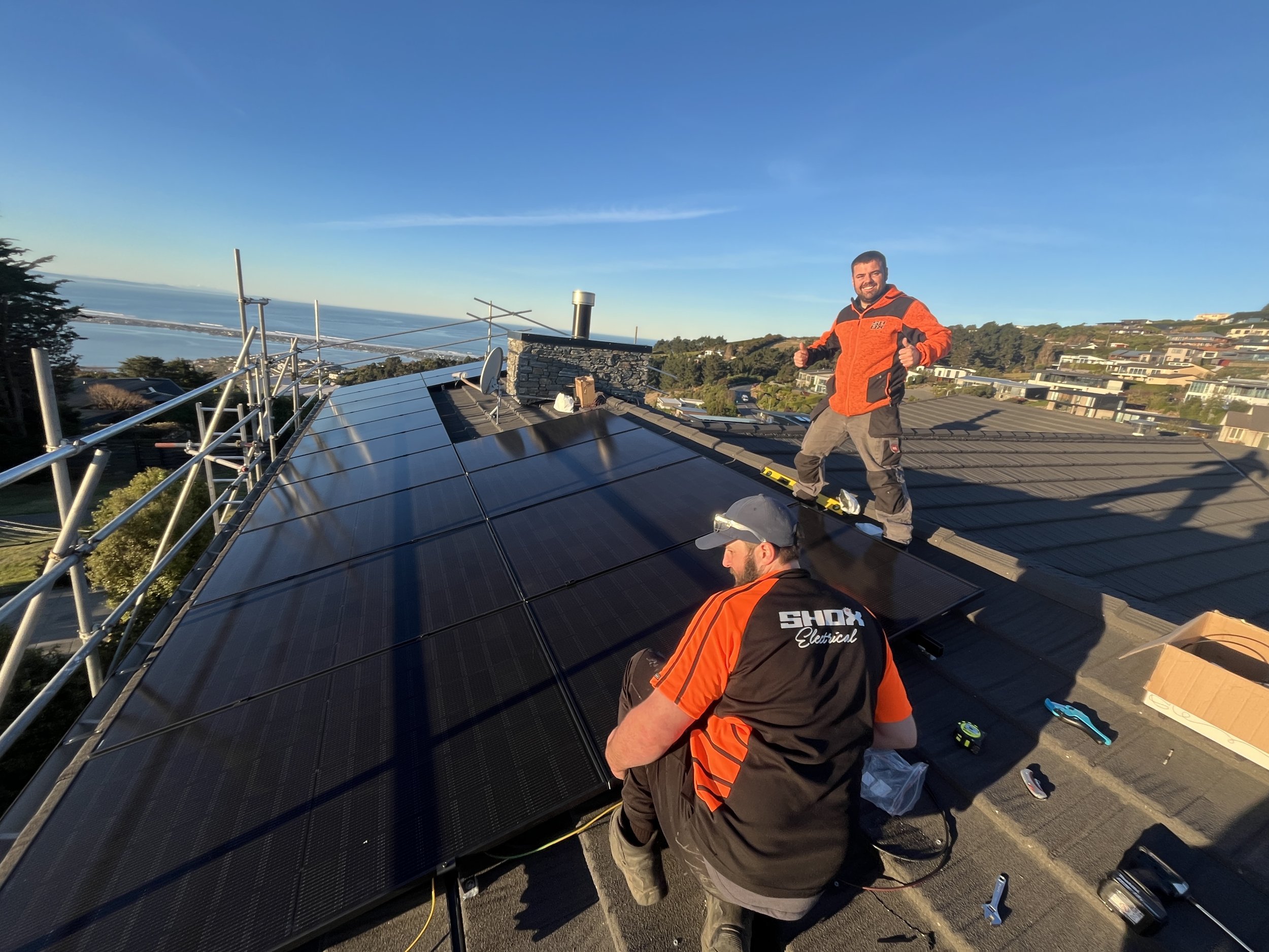 Shox Electrical team installing black solar panels on a Christchurch home with sea views