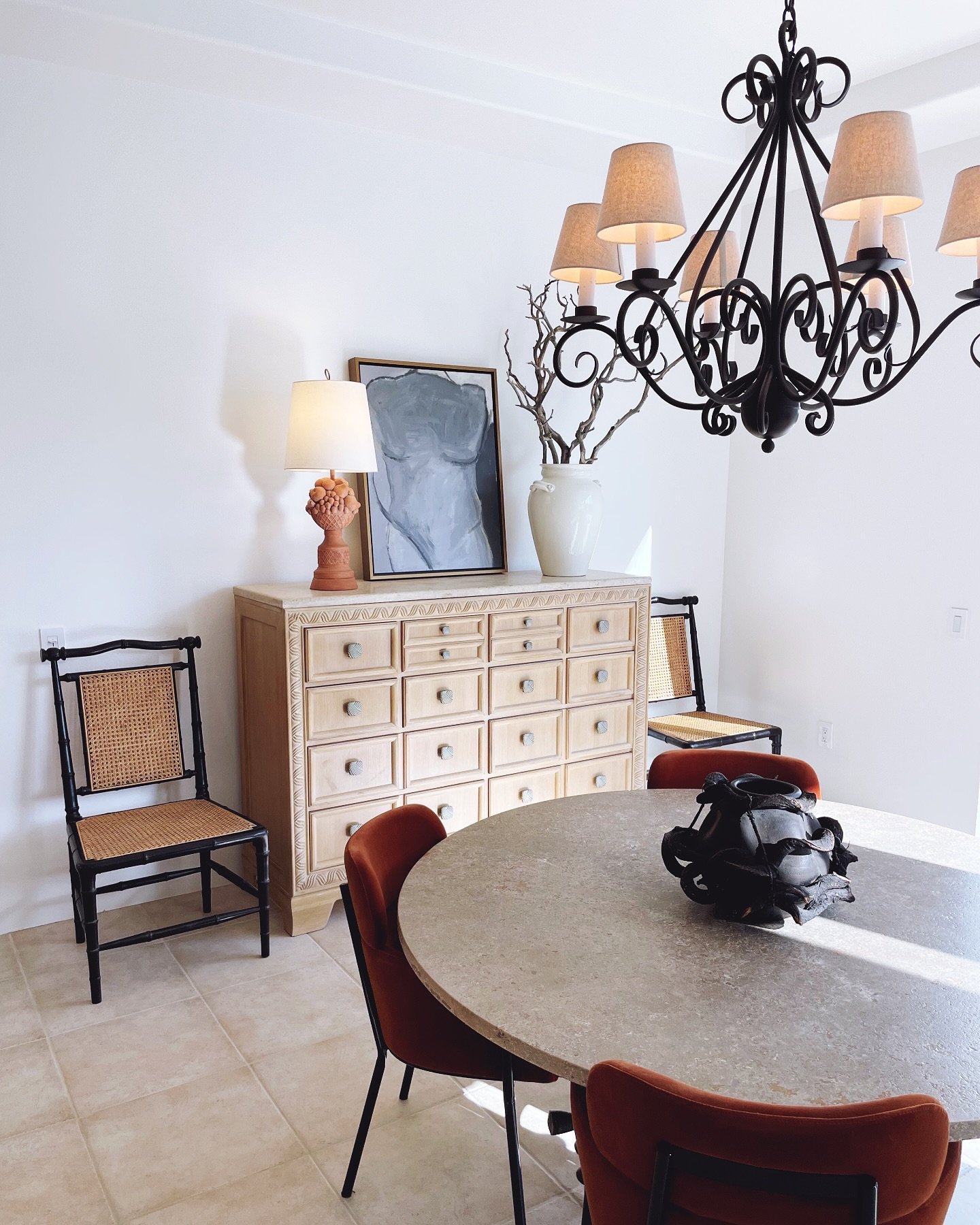 A hand-finished stone table anchors this La Quinta dining room, surrounded by rust velvet chairs for a pop of warmth against neutral tones. The art and ceramics were chosen for their soulful, imperfect beauty &mdash; a nod to the desert landscape jus