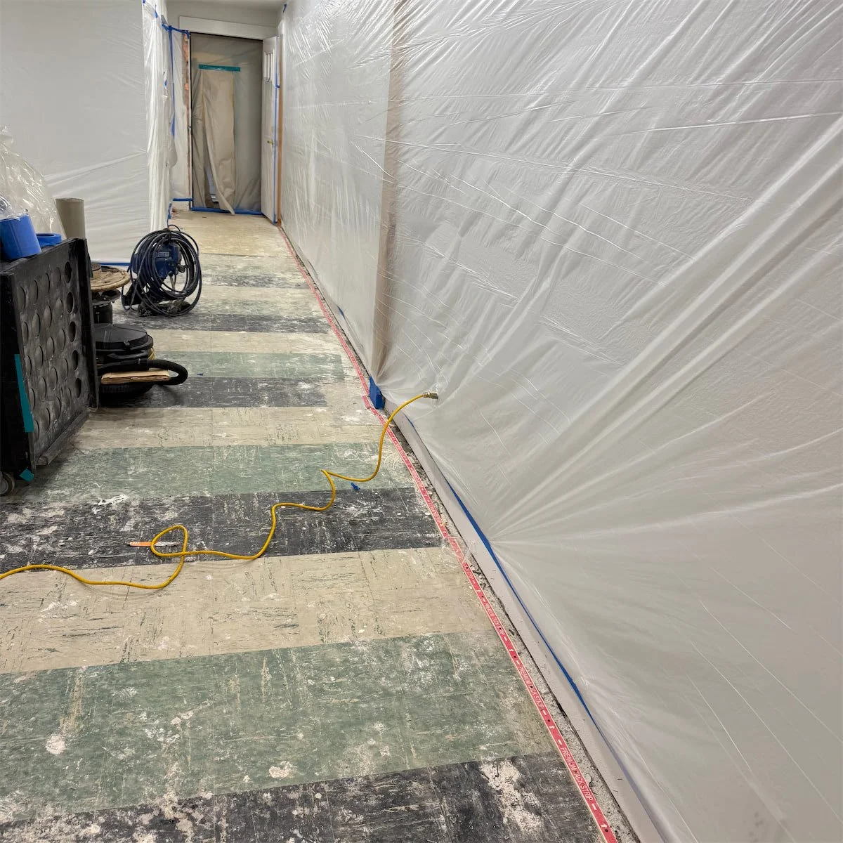 Interior corridor under renovation, with plastic sheeting on the wall, electrical cords, and tools on the floor.