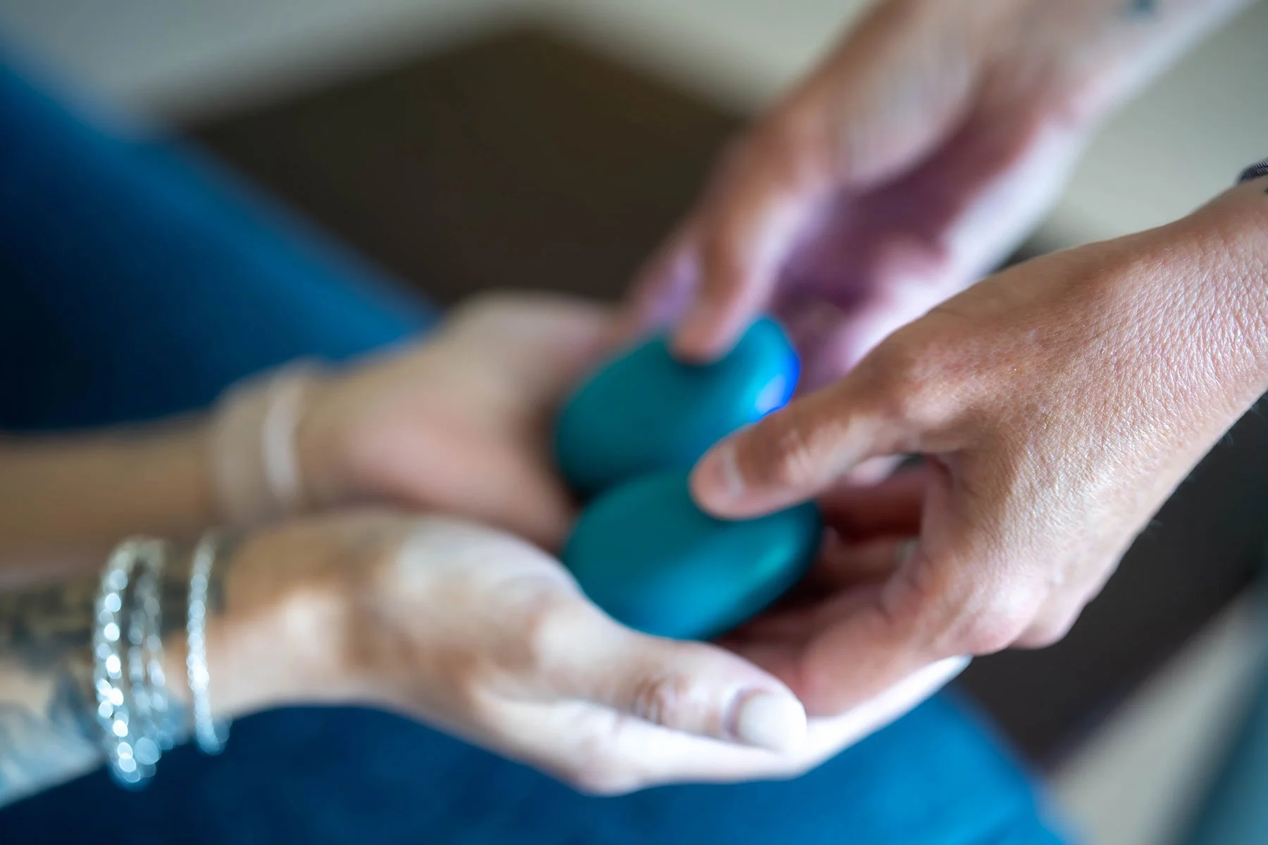 Close-up of a person's hands holding two teal-colored stones, wearing multiple rings and jewelry.