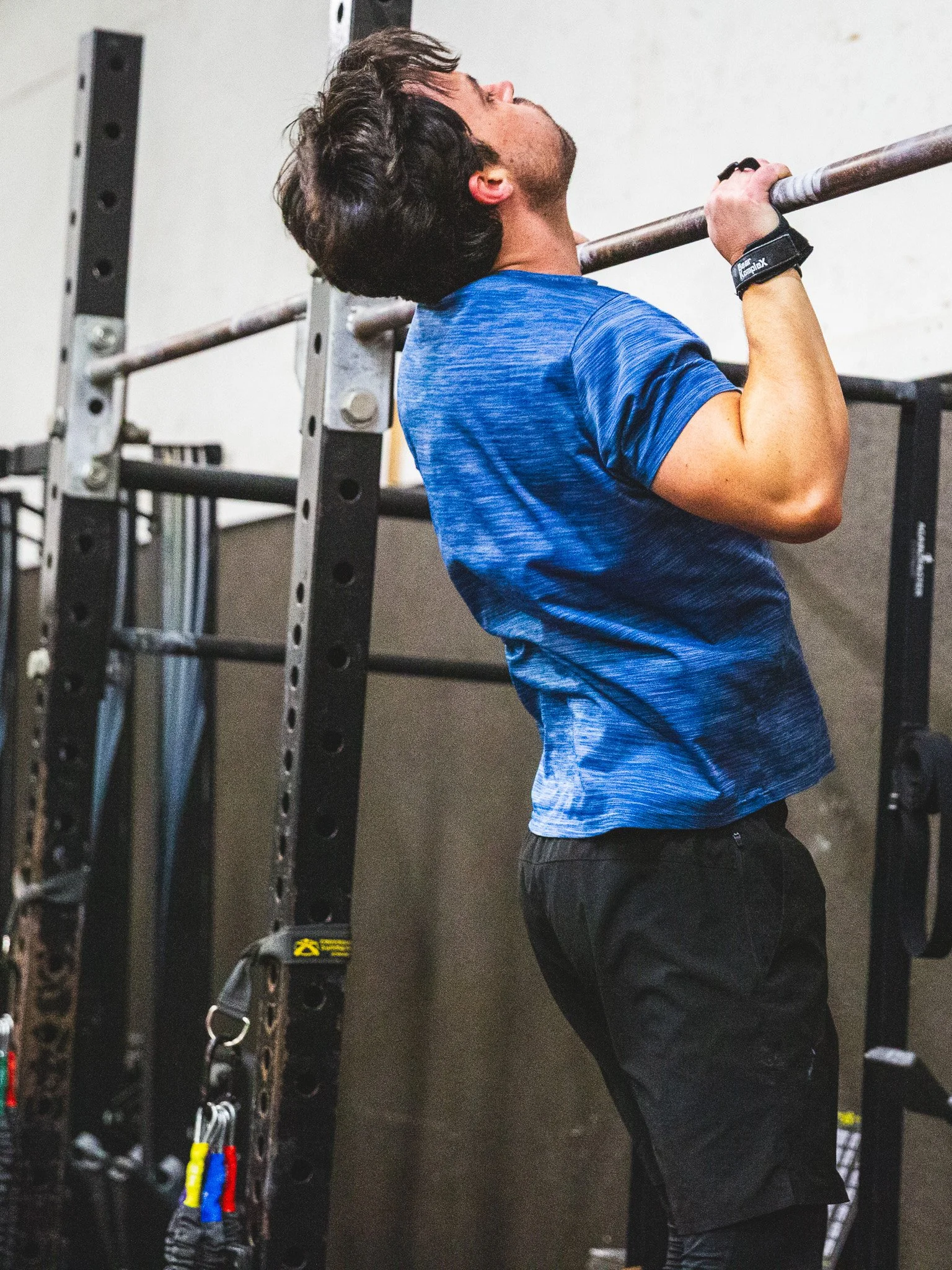 Young man in a blue shirt lifting a barbell in a gym.