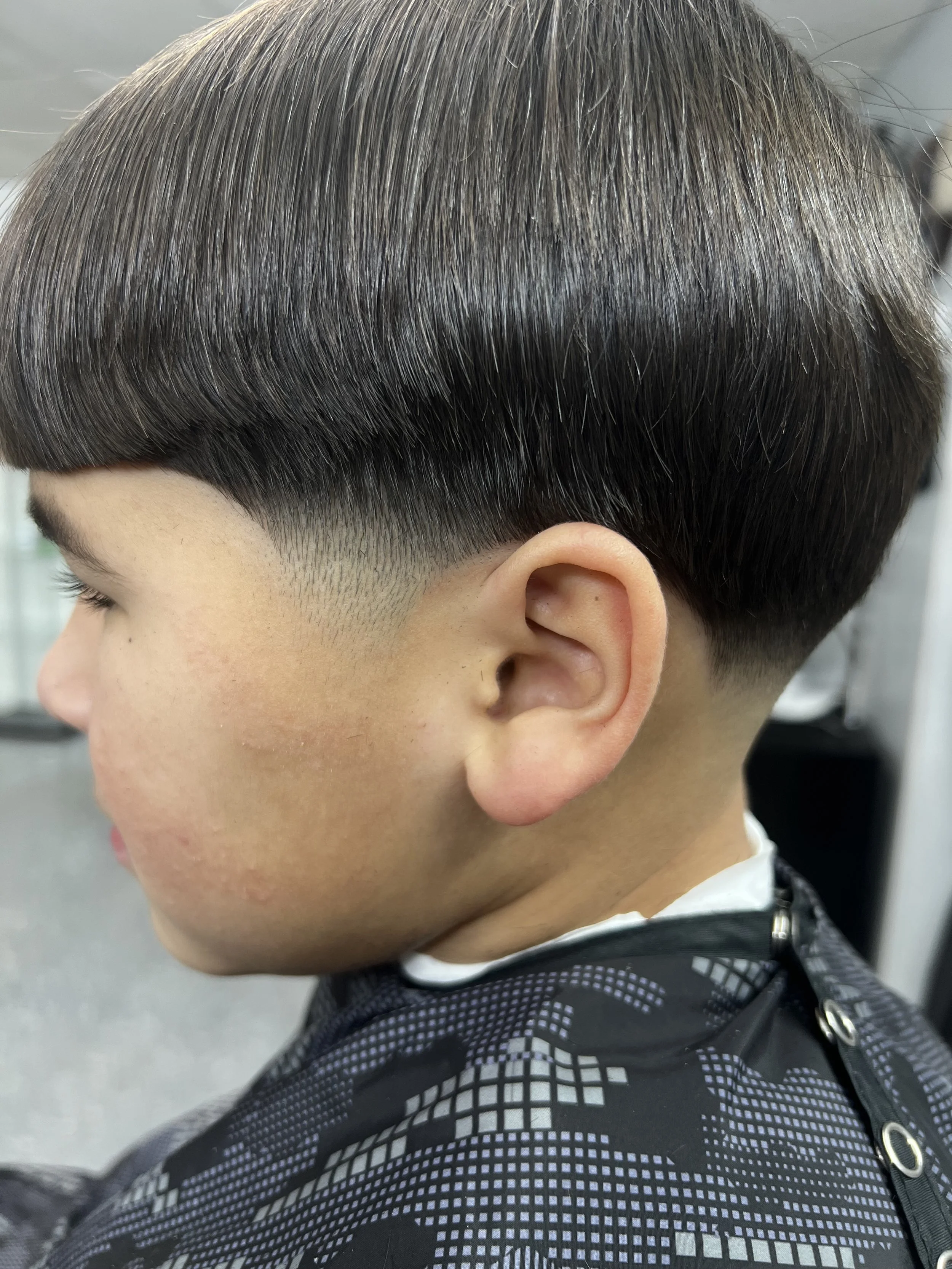 A close-up side view of a person with a bowl haircut, showing neatly trimmed dark hair.