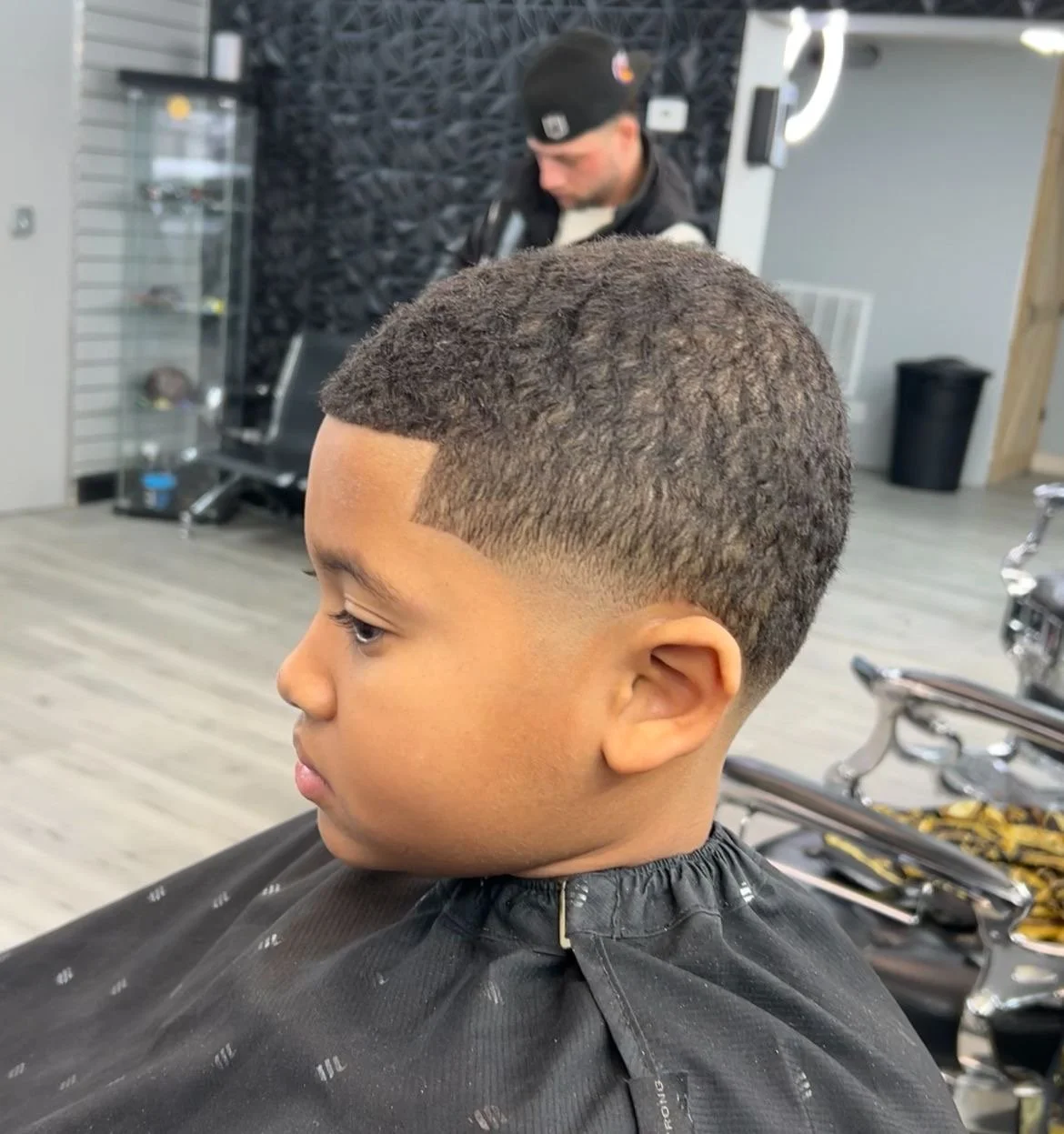 Young boy with a fresh fade hairstyle sitting on a barber chair in a barbershop.