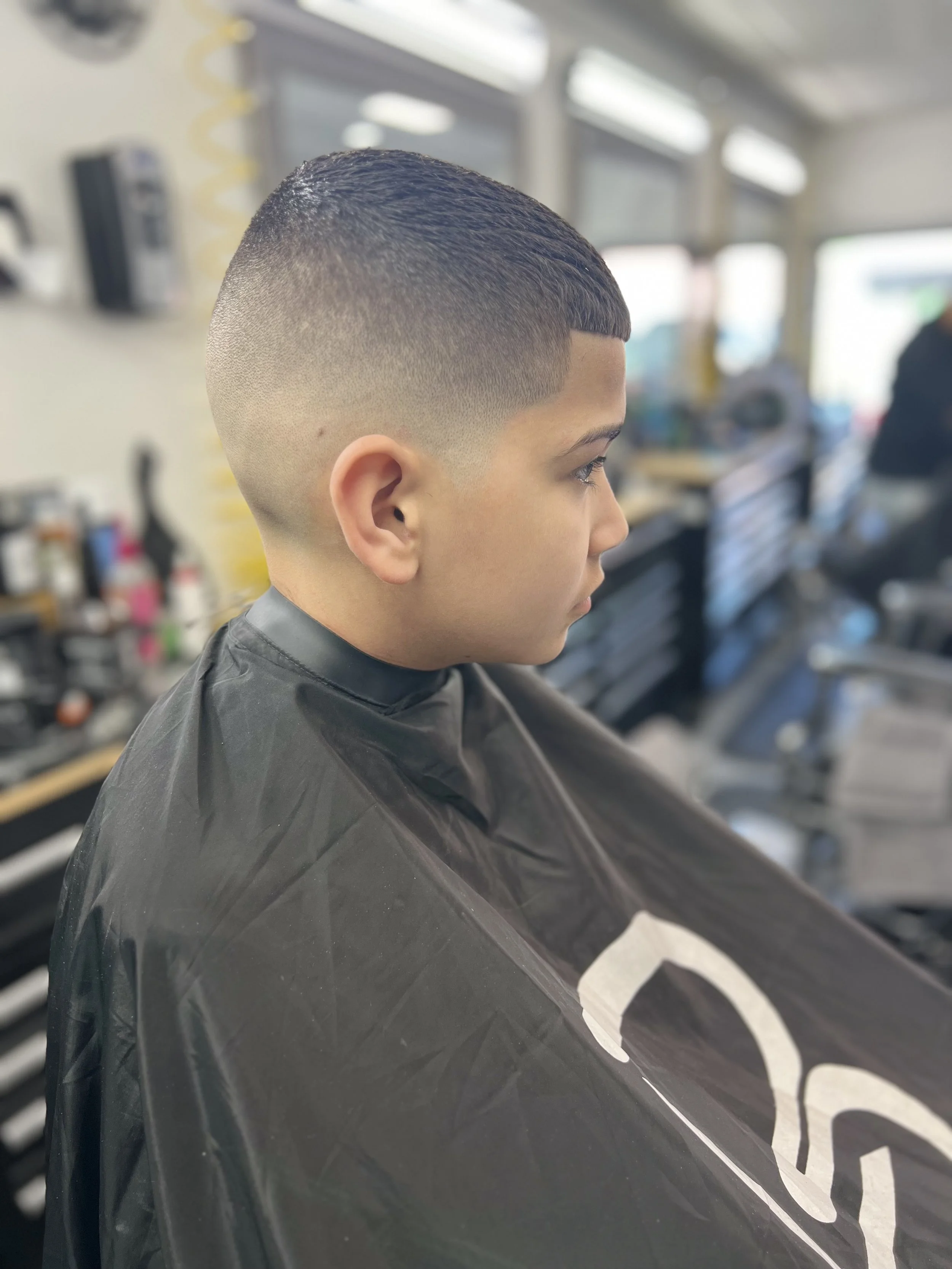 Boy with a fresh fade haircut sitting in a barbershop chair wearing a cape.
