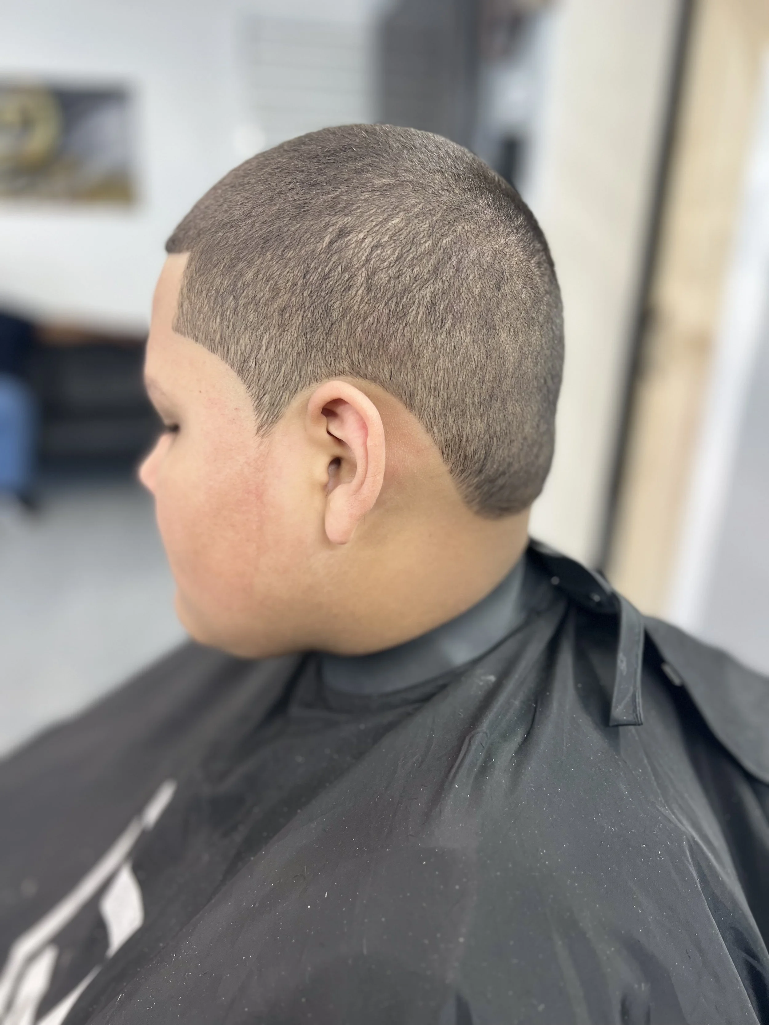 Side profile of a person with a buzz cut haircut, wearing a black barber cape.