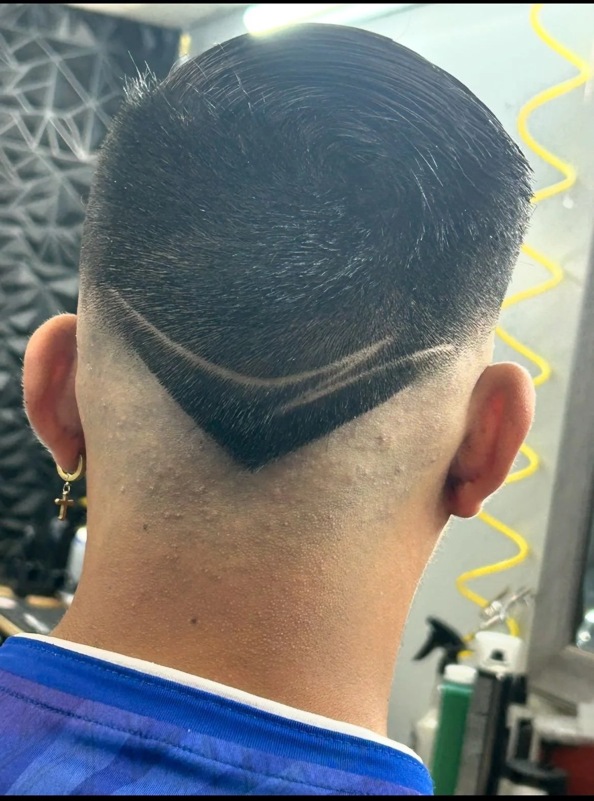 Person's back of the head with a geometric haircut design featuring sharp lines and angles at the nape.