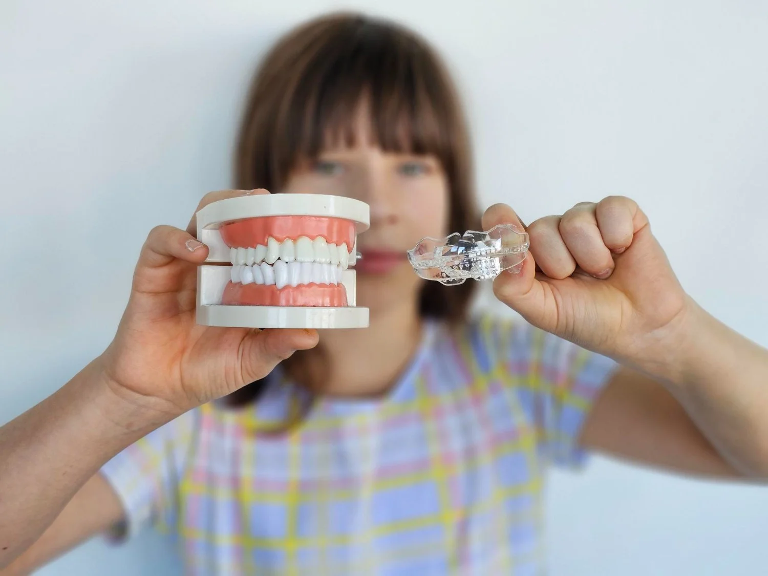 Woman holding a dental model and a clear dental aligner.