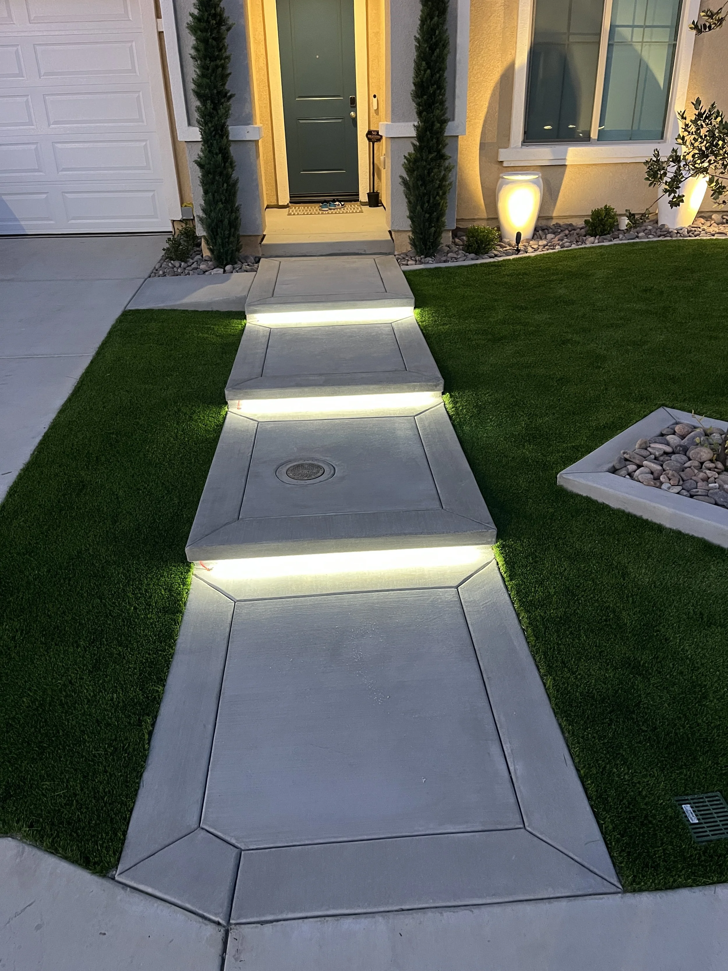Concrete walkway installation with artificial turf and integrated step lighting in Murrieta, CA, designed for a clean and modern front yard appearance.