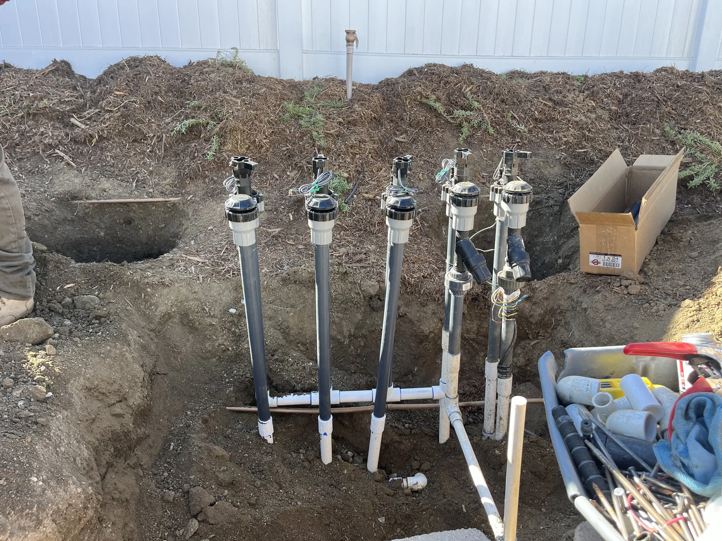 Underground water irrigation system installation with multiple pipes and valves in a dug-out hole.