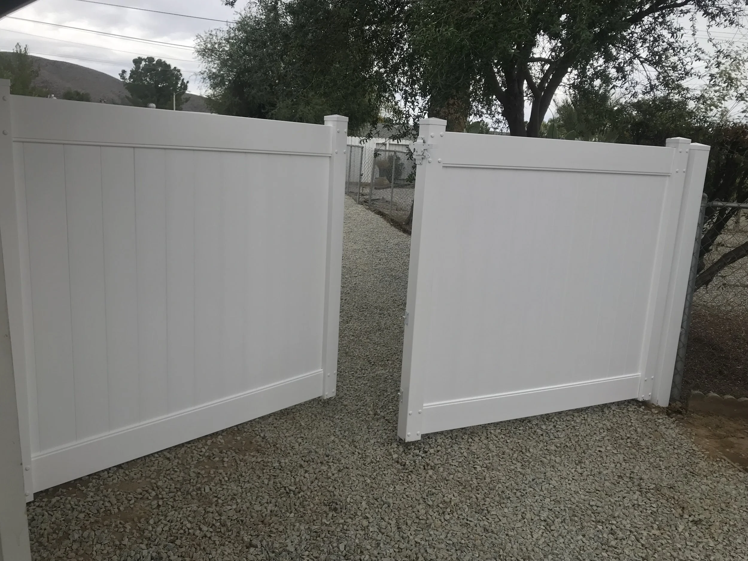 White double gate with gravel pathway behind, trees and overcast sky in the background.