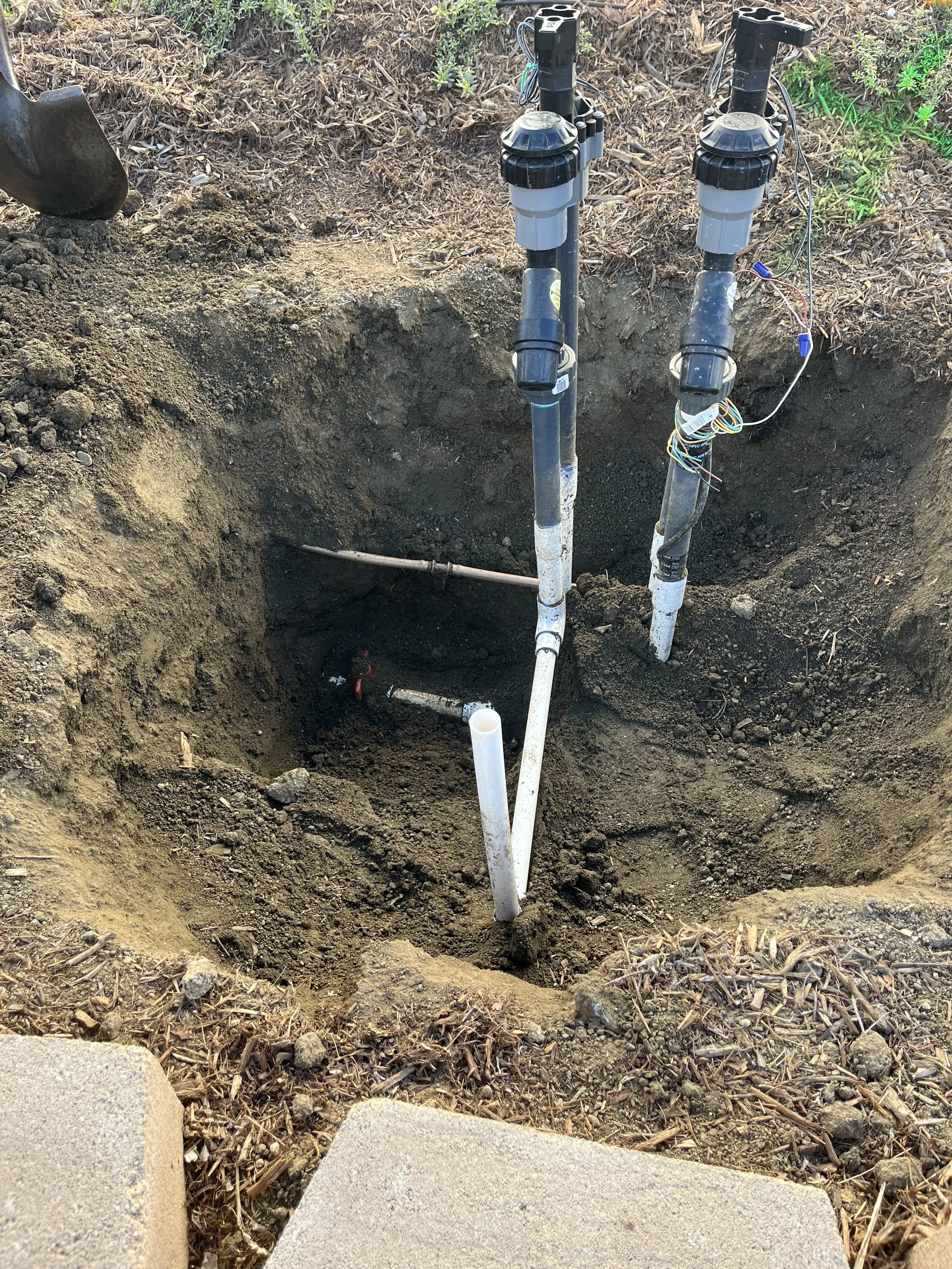 Underground water piping with two pipes and wiring at a construction site, surrounded by dirt and soil.