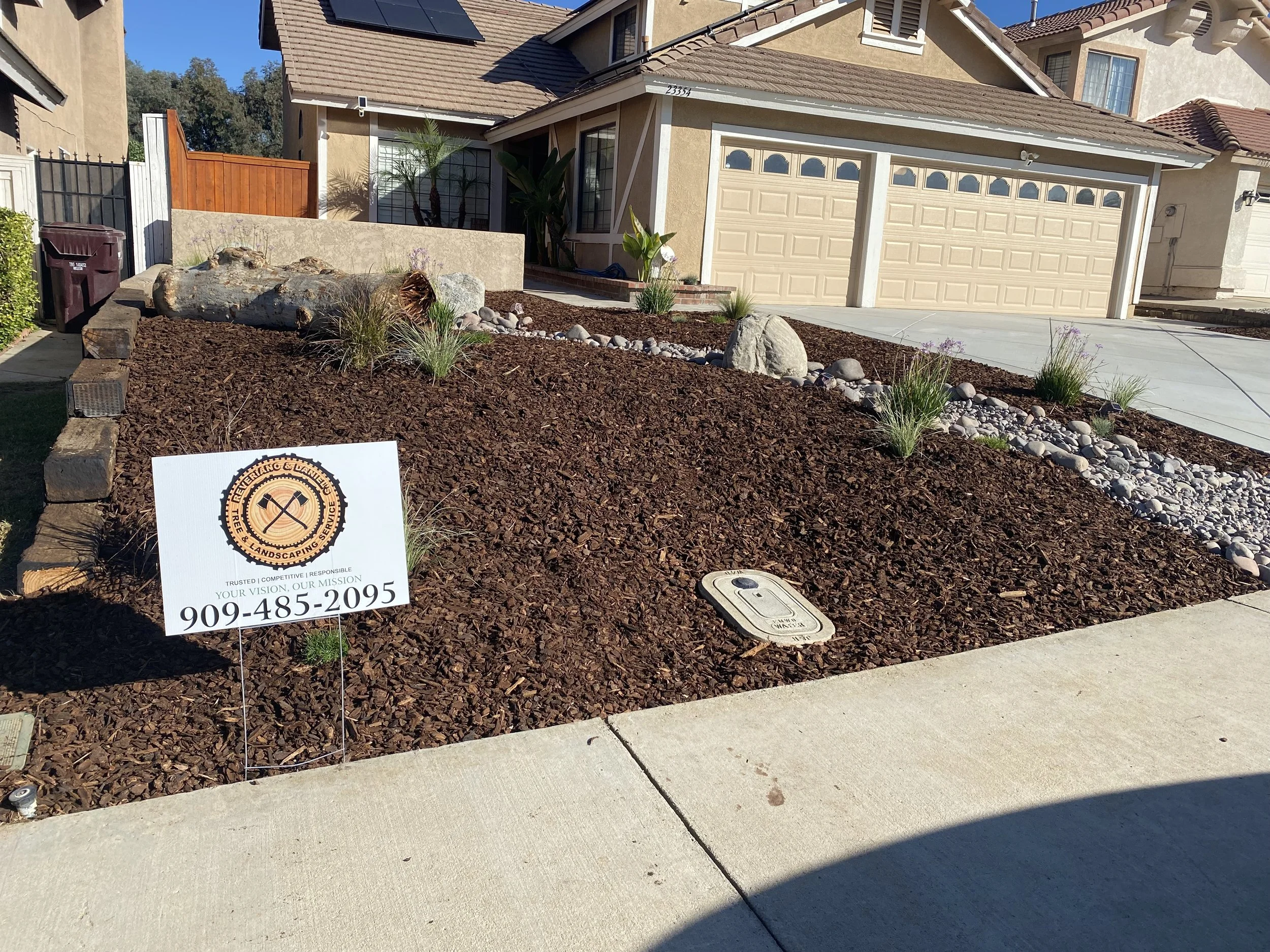 A freshly landscaped front yard with brown mulch, decorative rocks, and drought-tolerant plants in front of a suburban house landscape contractor near Menifee, CA.  Concrete contractor near Murrieta, CA