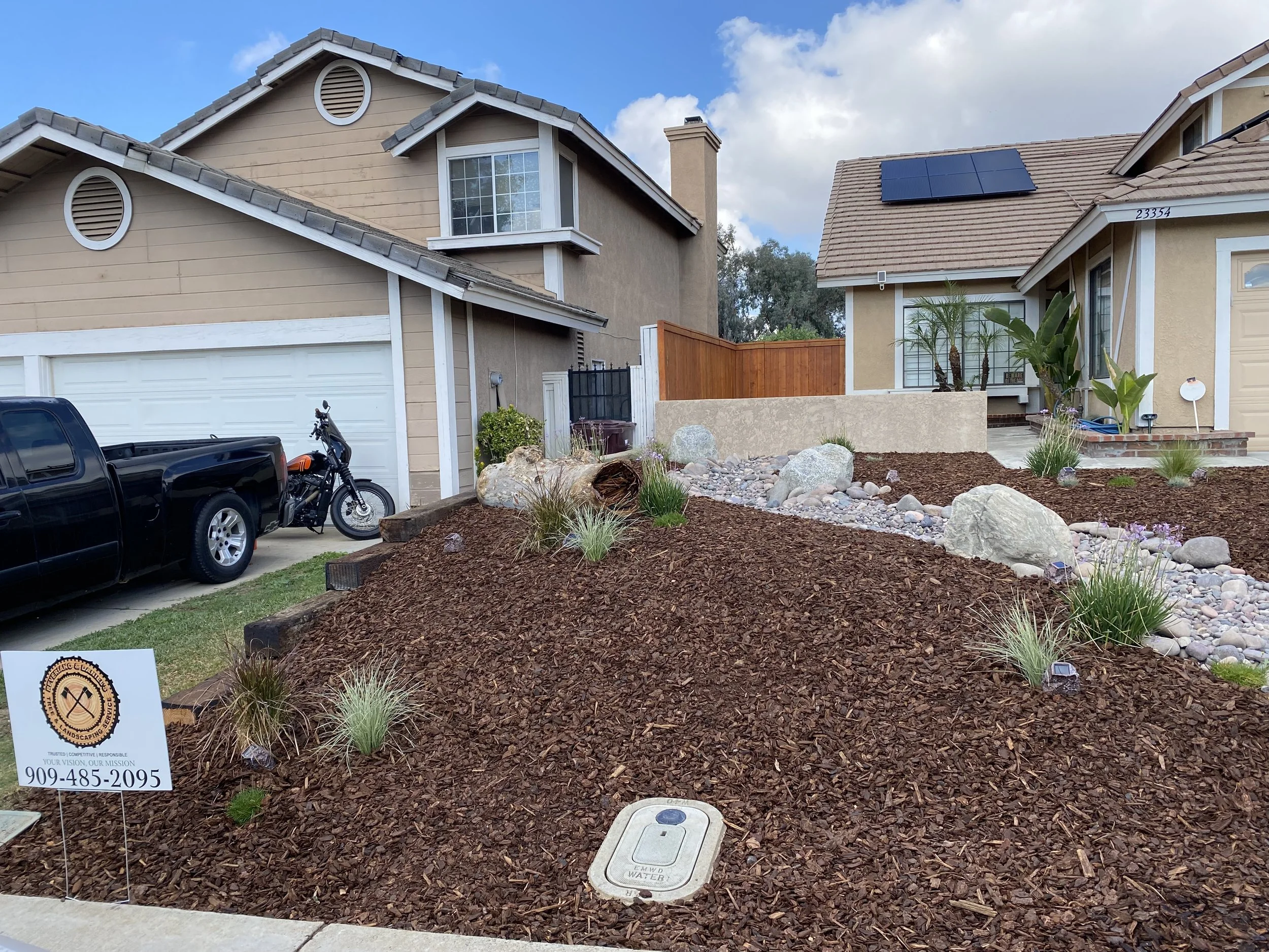 Front yard of a house with landscaped garden, rocks, and plants, including palm trees. The rock is called Arizona River Rock and Bark. The plants are California native grasses, in Moreno Valley