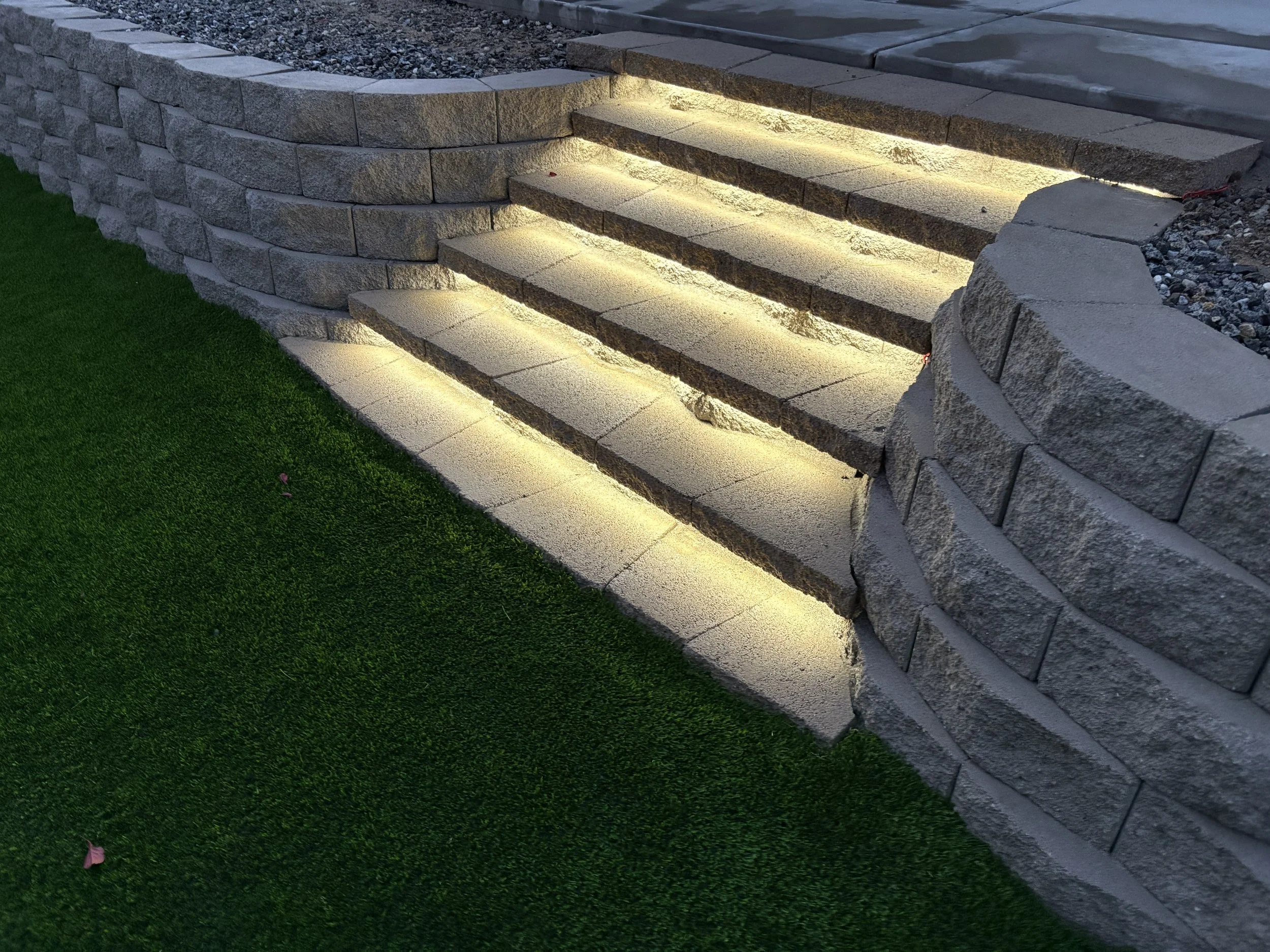 Stone staircase with built-in LED lighting, leading to a higher level, beside a lush green artificial grass lawn. Low-maintenance landscape with stone and turf – Canyon Lake