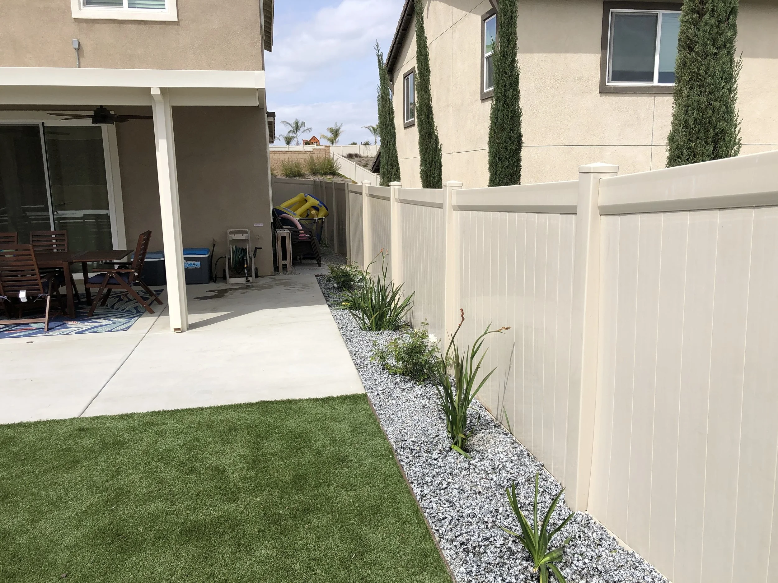 Backyard with a grassy lawn, concrete patio, beige privacy fence, and a row of tall, narrow cypress trees.  Decorative concrete and aloe landscape design – Menifee, CA