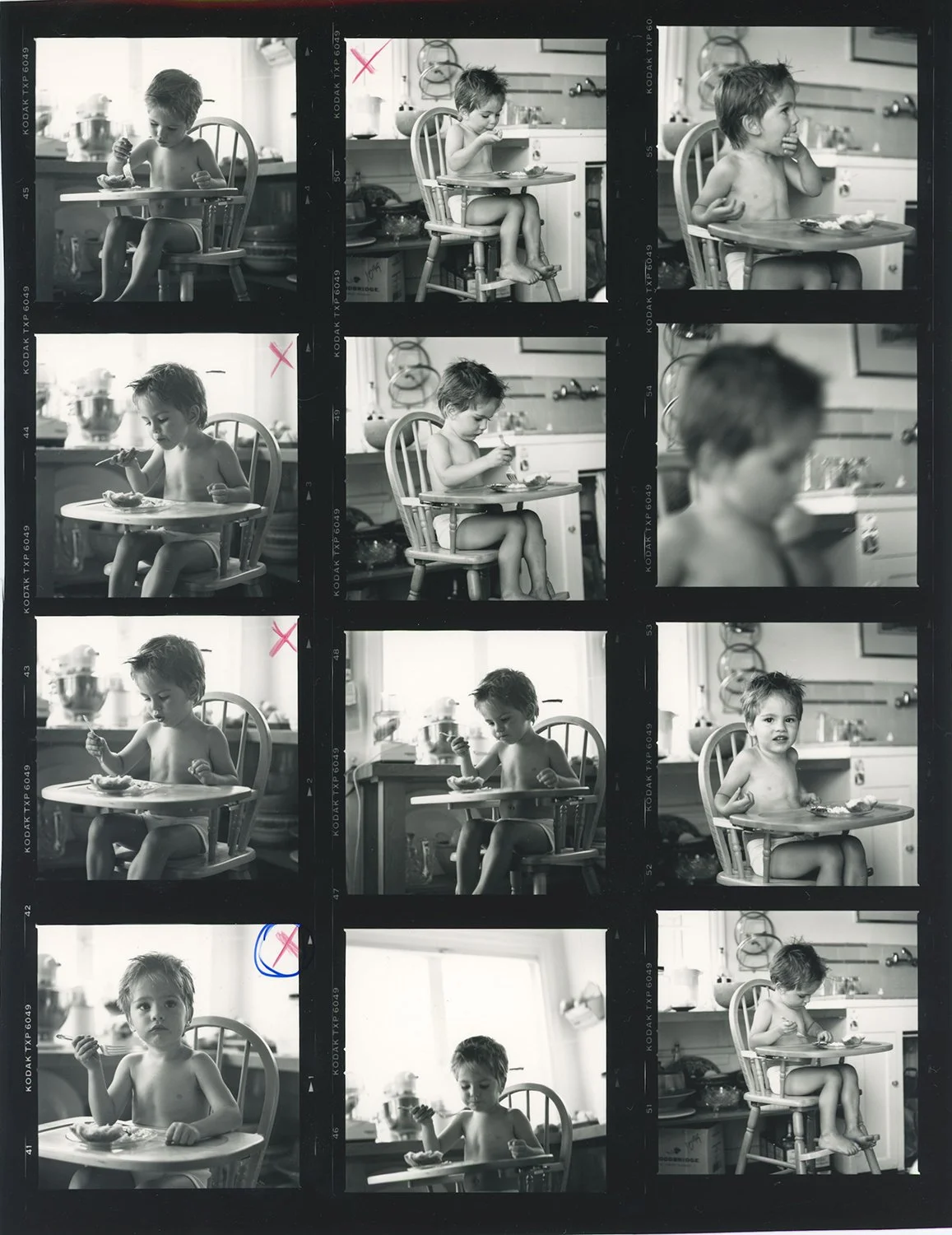 b&w photo of toddler sitting in high chair in kitchen eating a meal