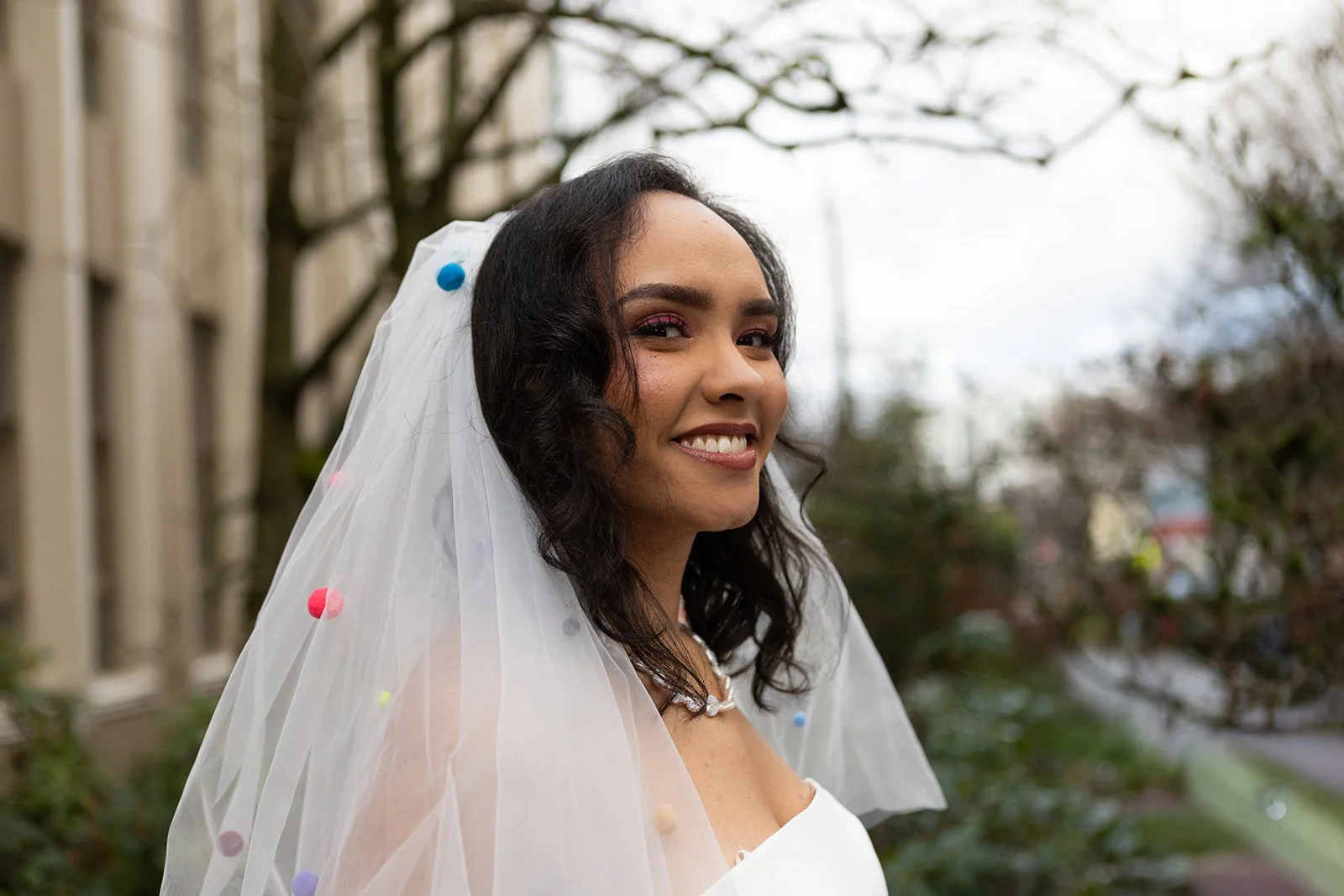 Outdoor bridal portrait of the bride smiling beneath a whimsical veil, photographed in soft natural light.