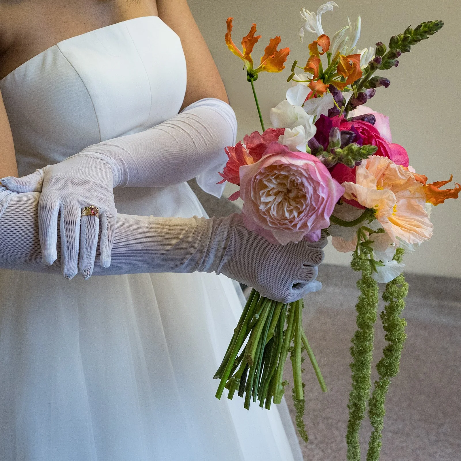 Wedding detail of the bride’s gloved hands holding a colorful bouquet, highlighting texture, florals, and personal style.