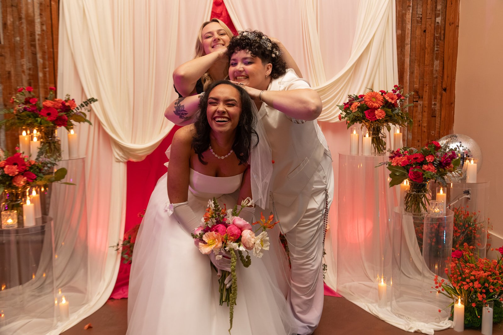 Bride and groom laughing with a friend during a playful wedding portrait in front of a colorful ceremony backdrop.
