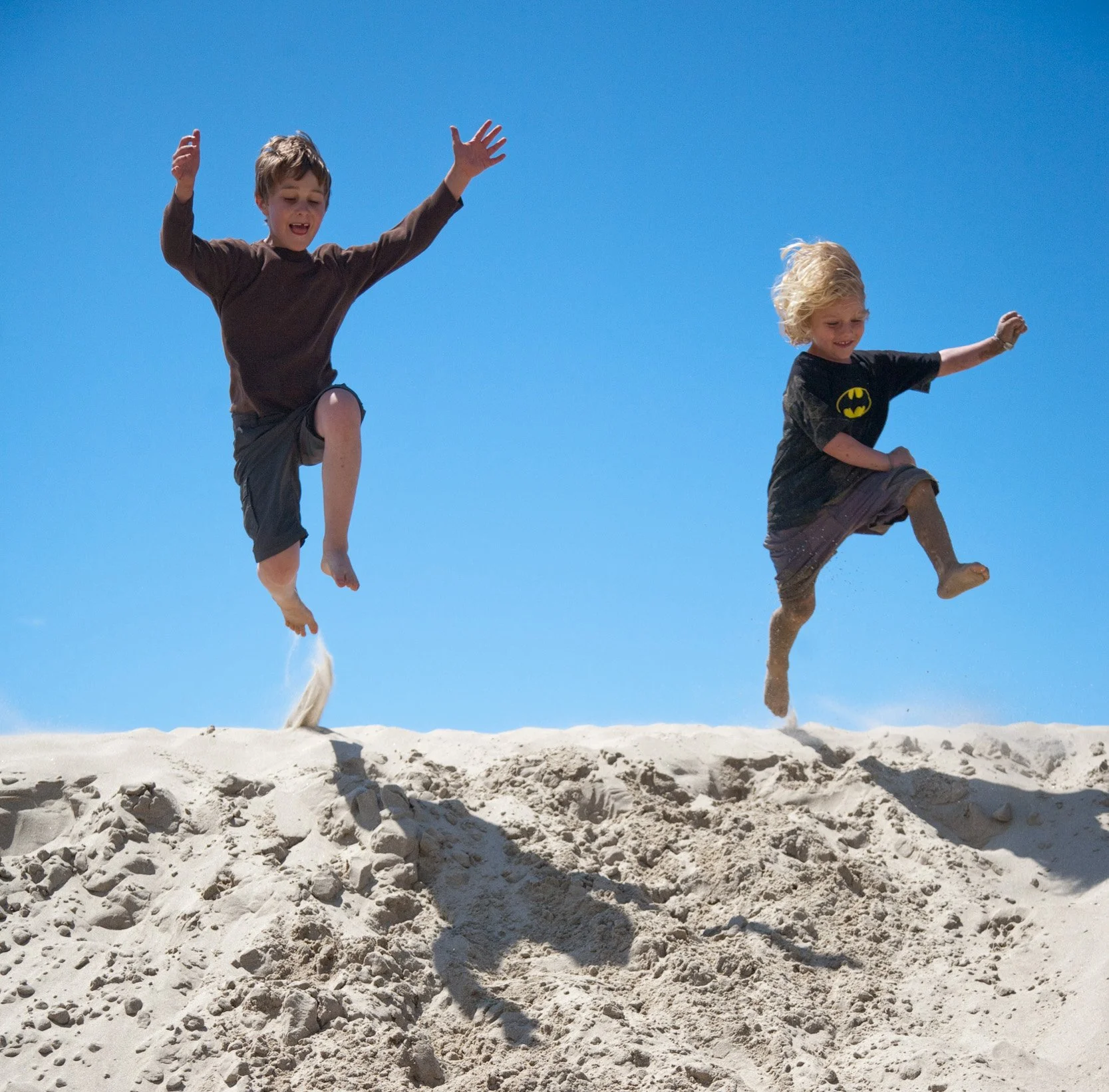 Kids jumping from sand dunes in summer.