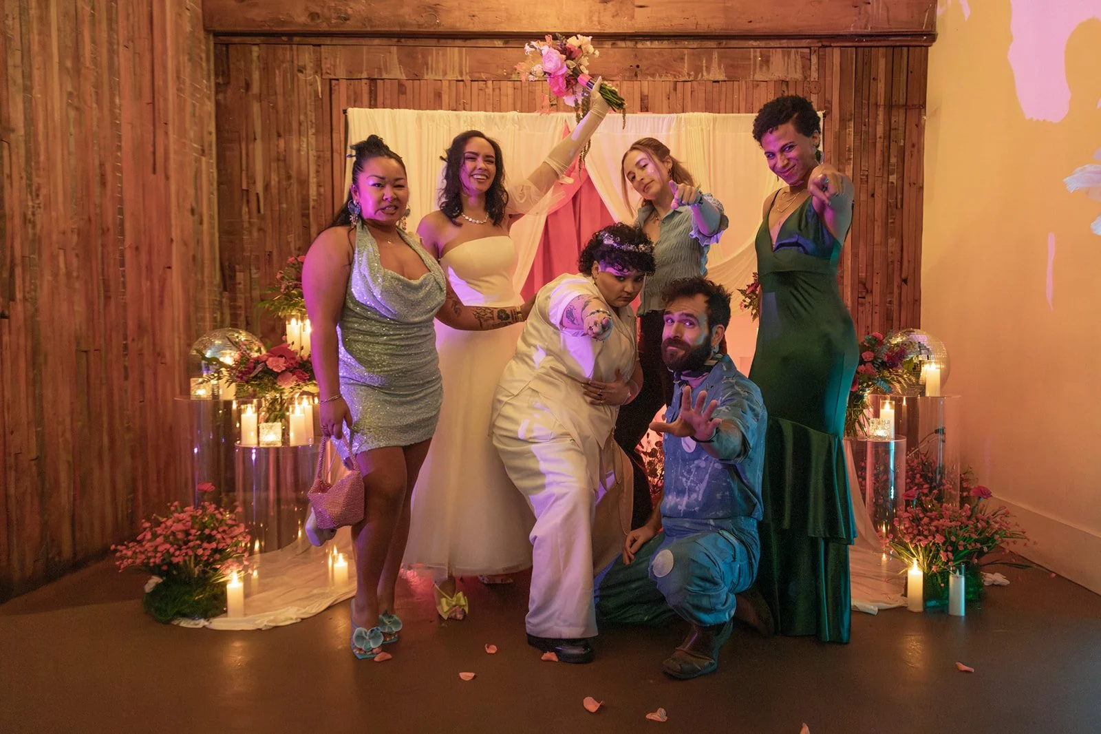 Bride and groom posing with friends in a joyful, inclusive wedding party portrait during the celebration.