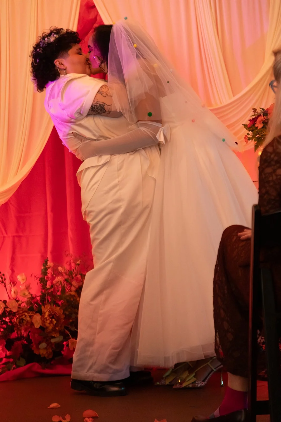 Bride and groom sharing their first kiss during a joyful LGBTQ wedding ceremony in warm, vibrant light.