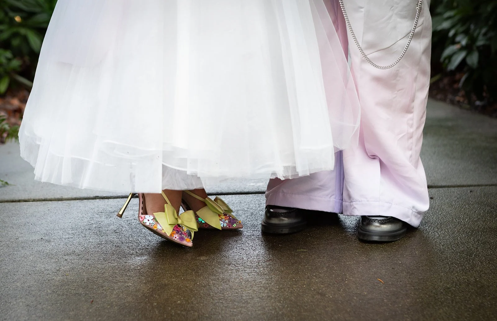 Wedding detail of the bride and groom’s shoes beneath a flowing dress, highlighting personal style and playful color.