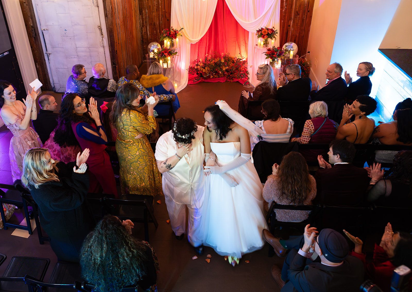 Overhead view of the bride and groom walking down the aisle as guests applaud during a joyful, inclusive wedding ceremony.