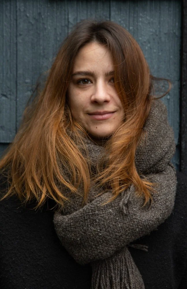 woman wearing chunky scarf against textured wall during a windy day, with her hair in motion. Seattle, WA