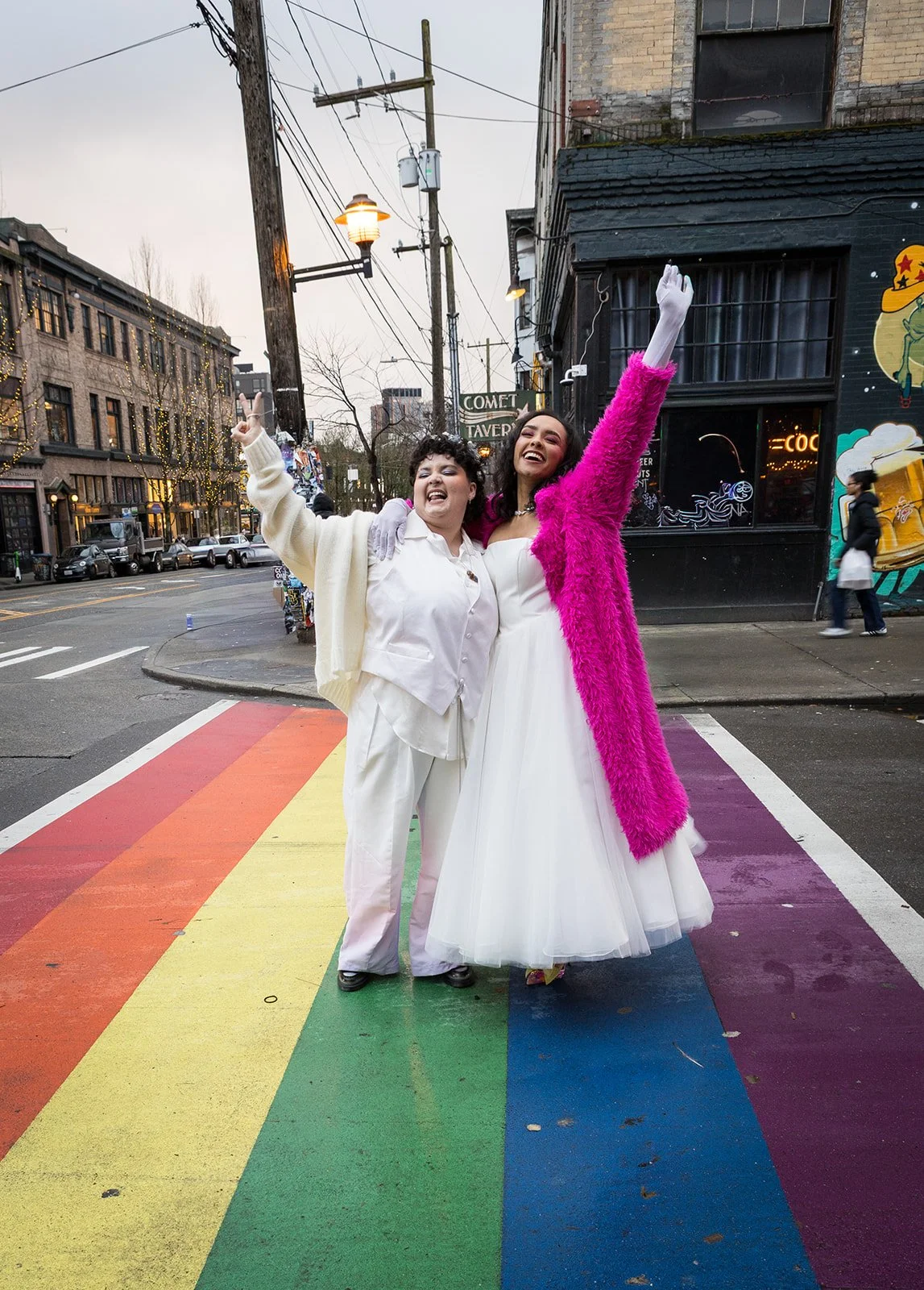 Bride and groom celebrating together on a rainbow crosswalk after their wedding, joyful and carefree city moment.