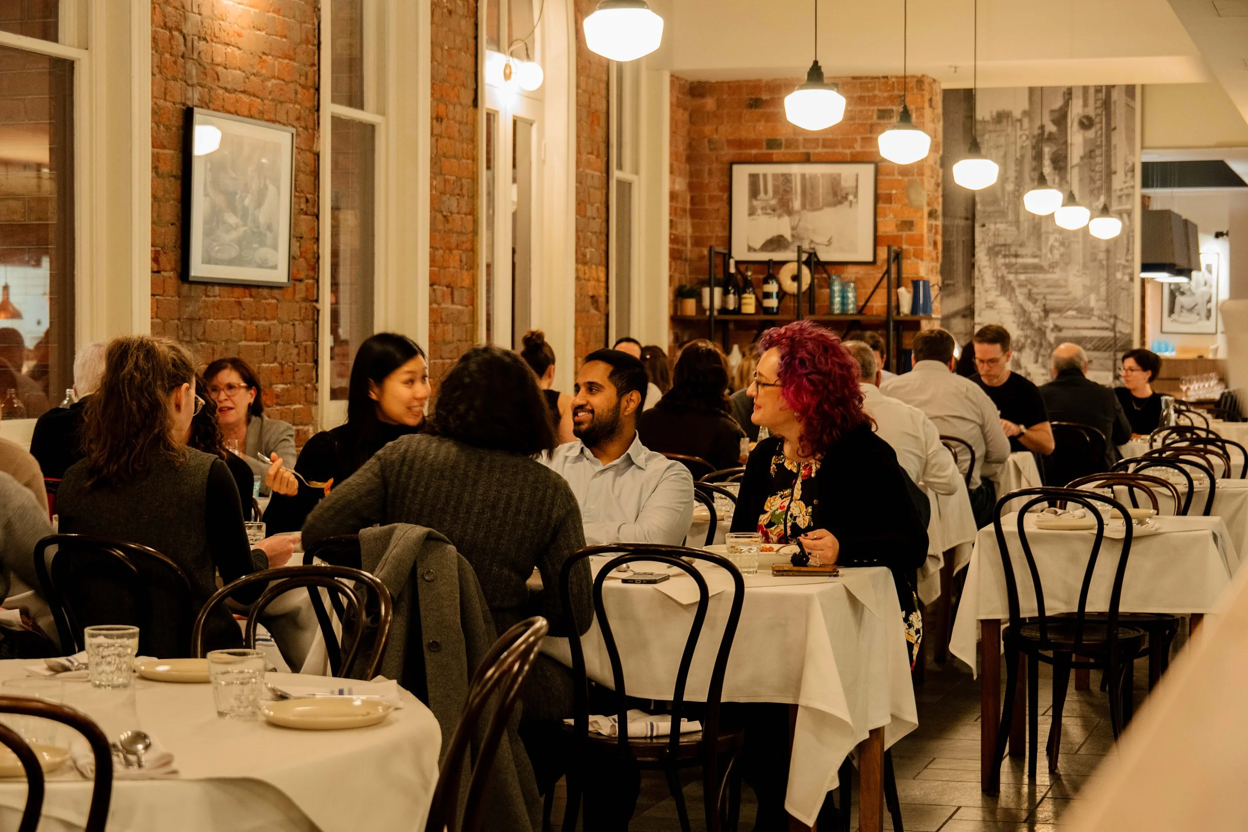 A full dining room at Ronnie’s, with white tablecloths, brick walls and pendant lights