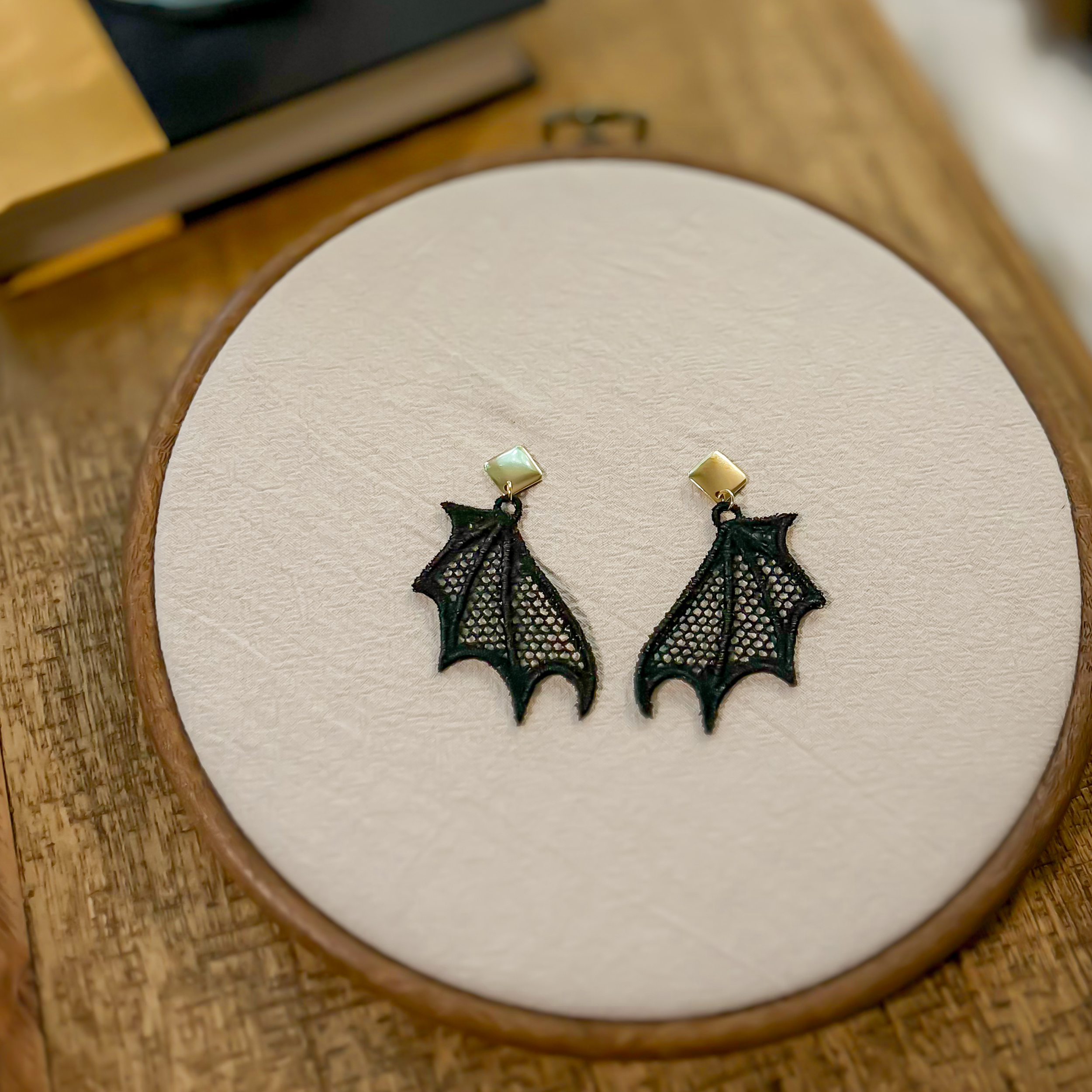 Freestanding lace bat wing earrings with black embroidery and gold studs, shown against a bright background to highlight lace detail.