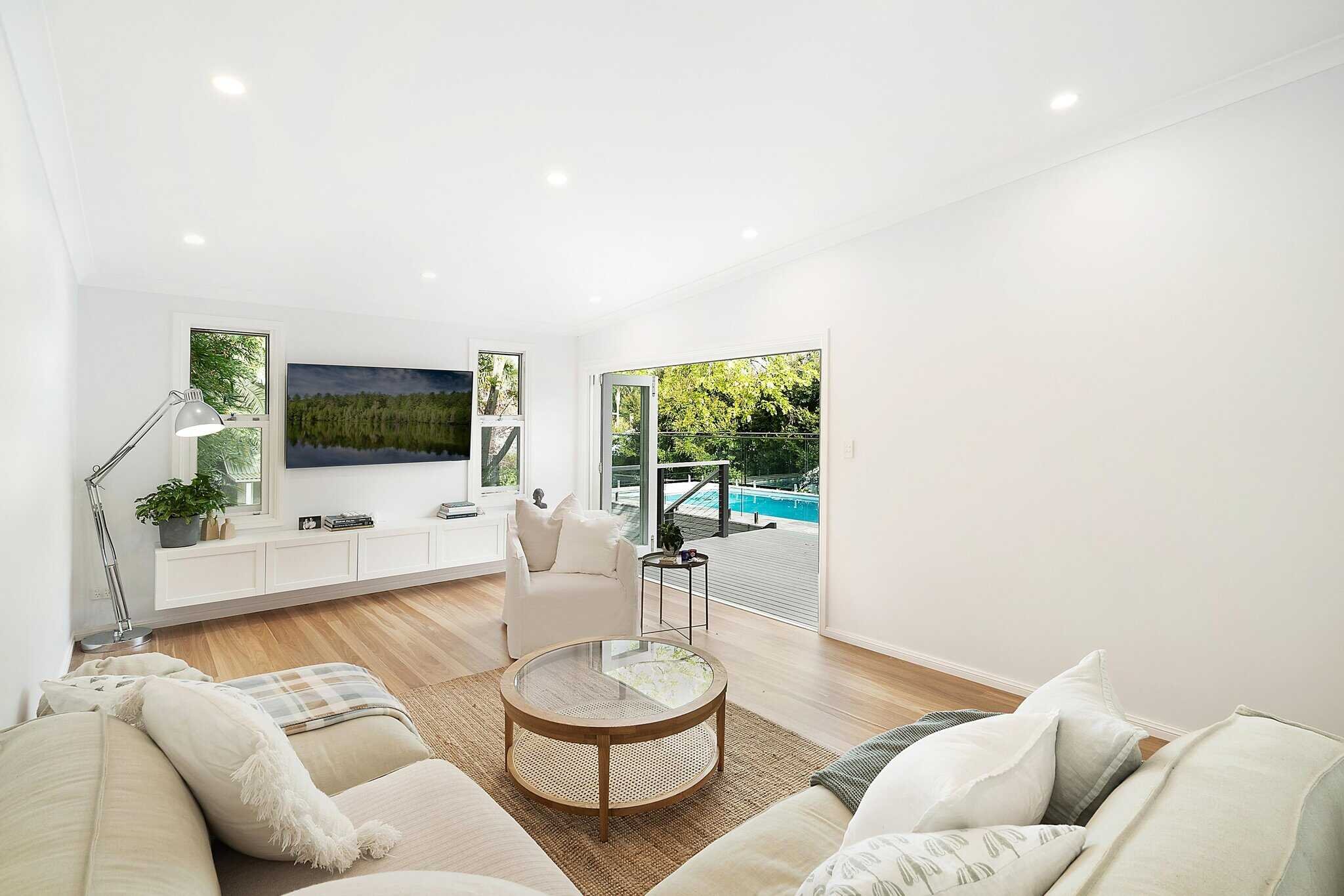 Modern living room with beige sofas, a round glass coffee table, and a view of the pool through open sliding doors.