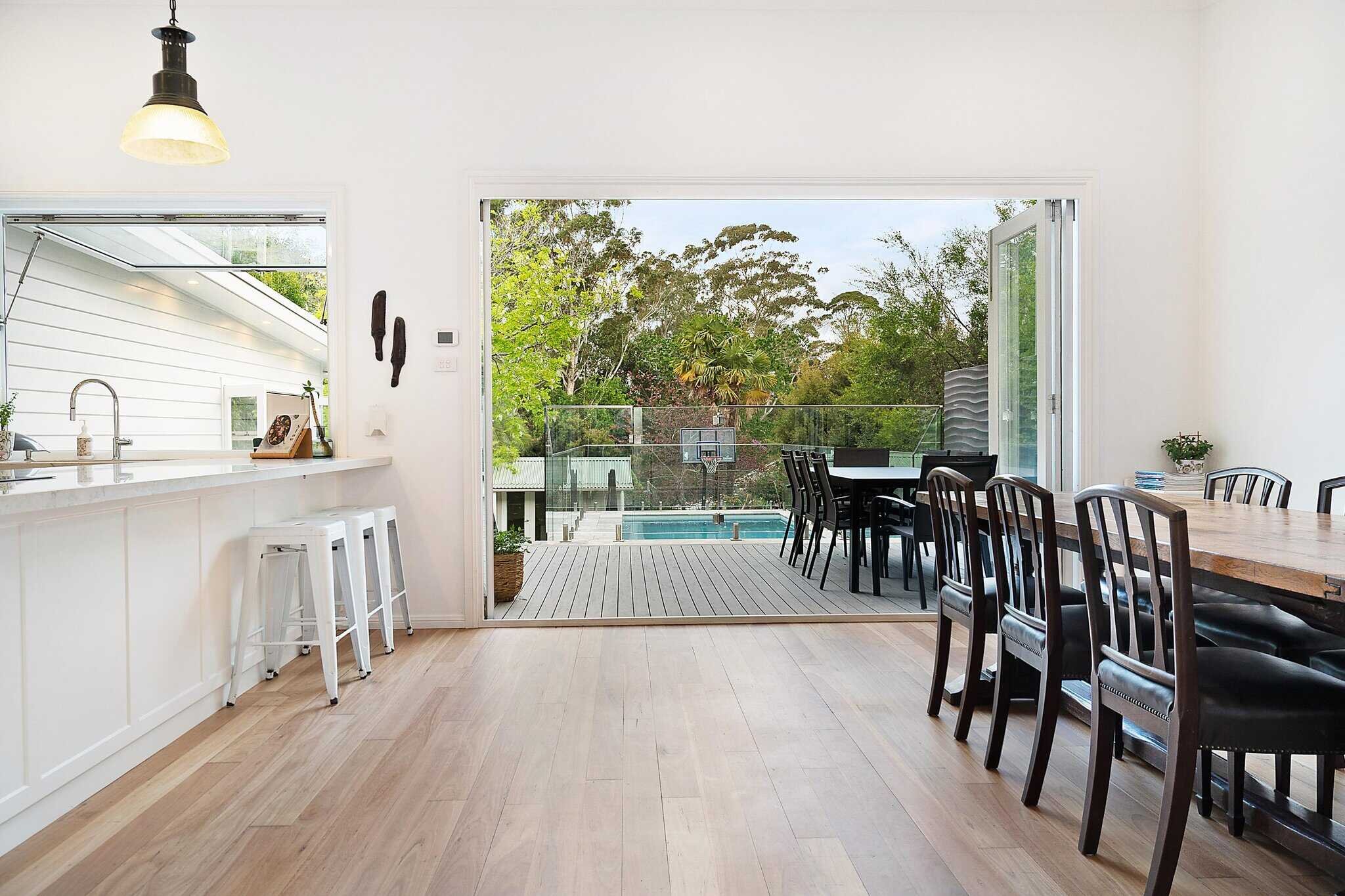 Modern kitchen and dining area with open sliding doors leading to a patio and swimming pool.