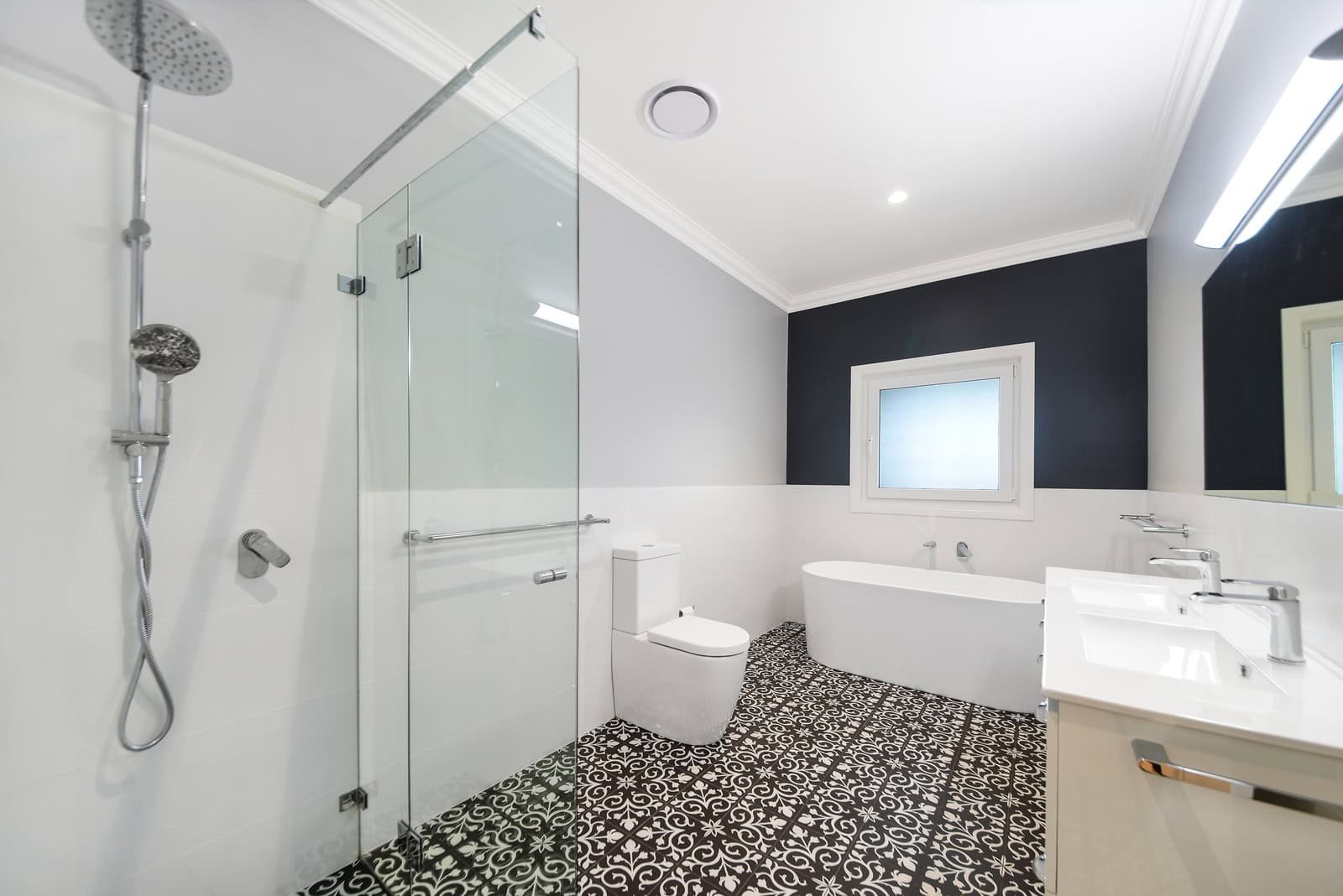 Modern bathroom with a glass-enclosed shower, freestanding bathtub, toilet, and dual-sink vanity. The floor features black and white patterned tiles.