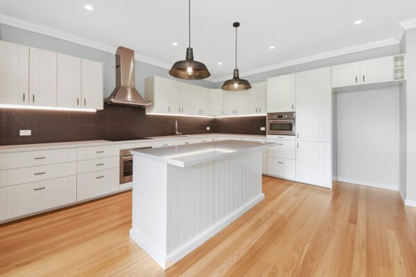 Modern kitchen with white cabinets, wooden floor, and a center island under pendant lights.