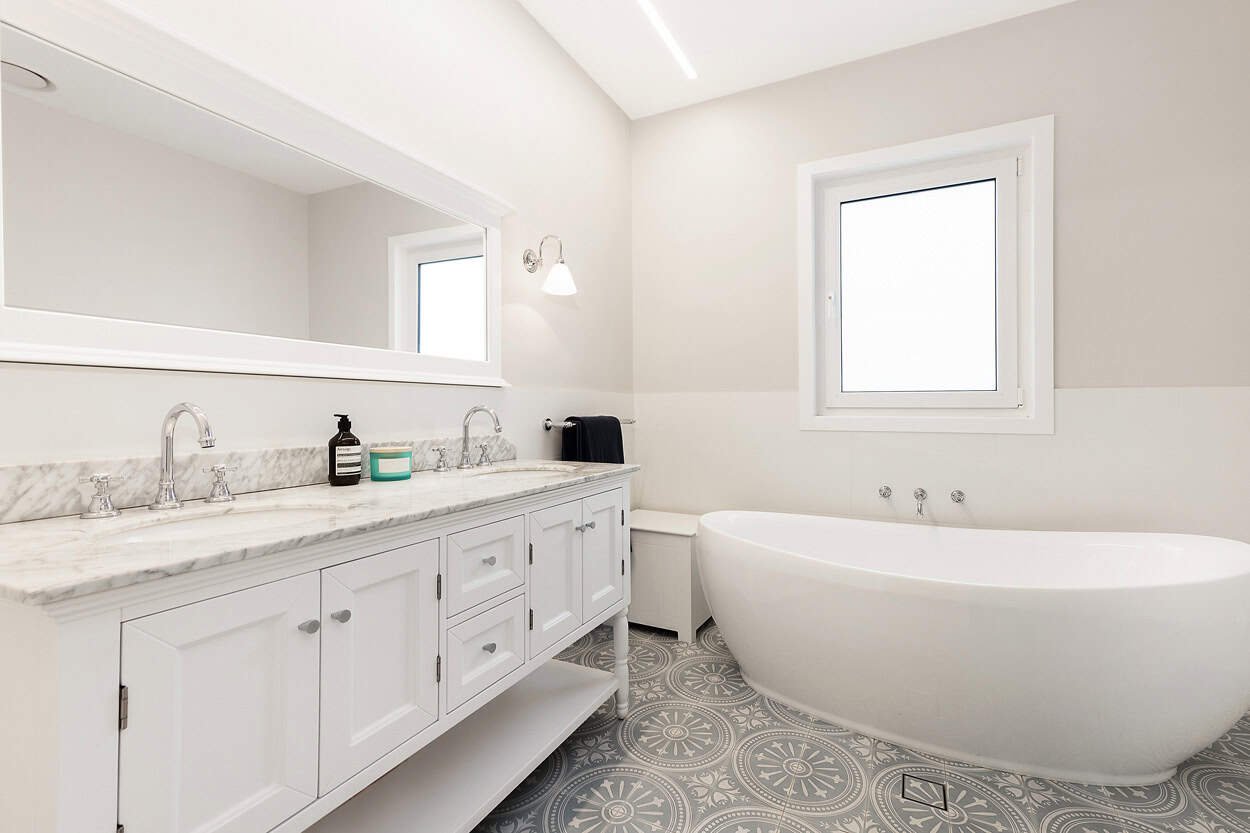Modern bathroom with freestanding bathtub, double sink vanity with marble countertop, large mirror, and decorative floor tiles.