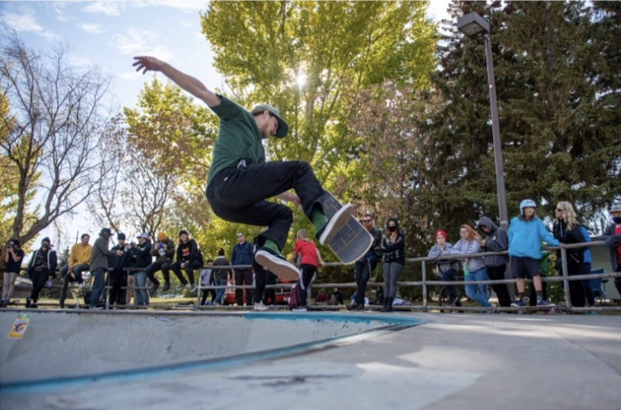 Young skateboarder performing a kickflip trick at a skatepark while a crowd watches.