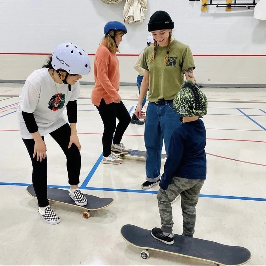 Group of people in a Right To Skate skateboarding class inside an indoor skate rink, with an instructor and children wearing helmets.
