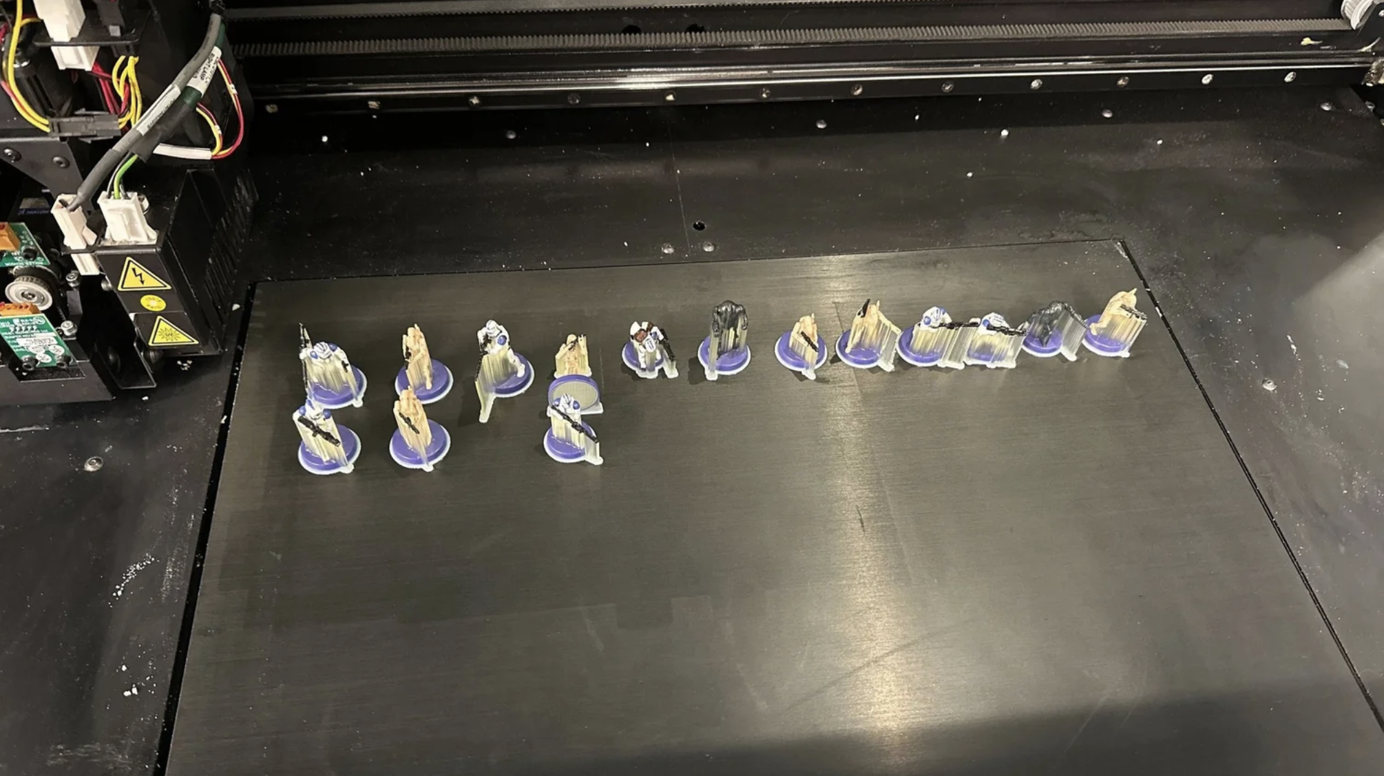 A 3D printer with several small parts being printed on the black printing bed.